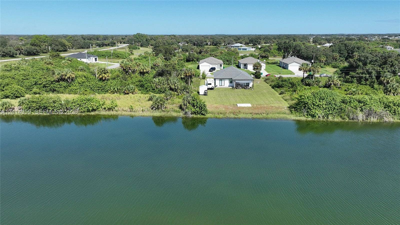 8017 Sunrise Circle, Labelle, FL 33935 Waterfront property featuring a landscaped lawn, paved driveway, and shingle-roof structure