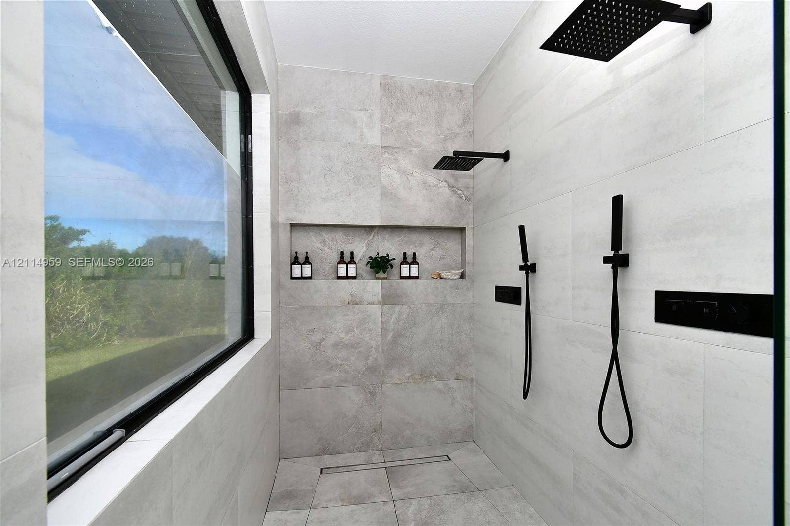 8017 Sunrise Circle, Labelle, FL 33935 Walk-in shower featuring large-format tile surround, matte black rainfall showerhead, dual handheld sprayers, built-in wall niche, and floor-to-ceiling glass window