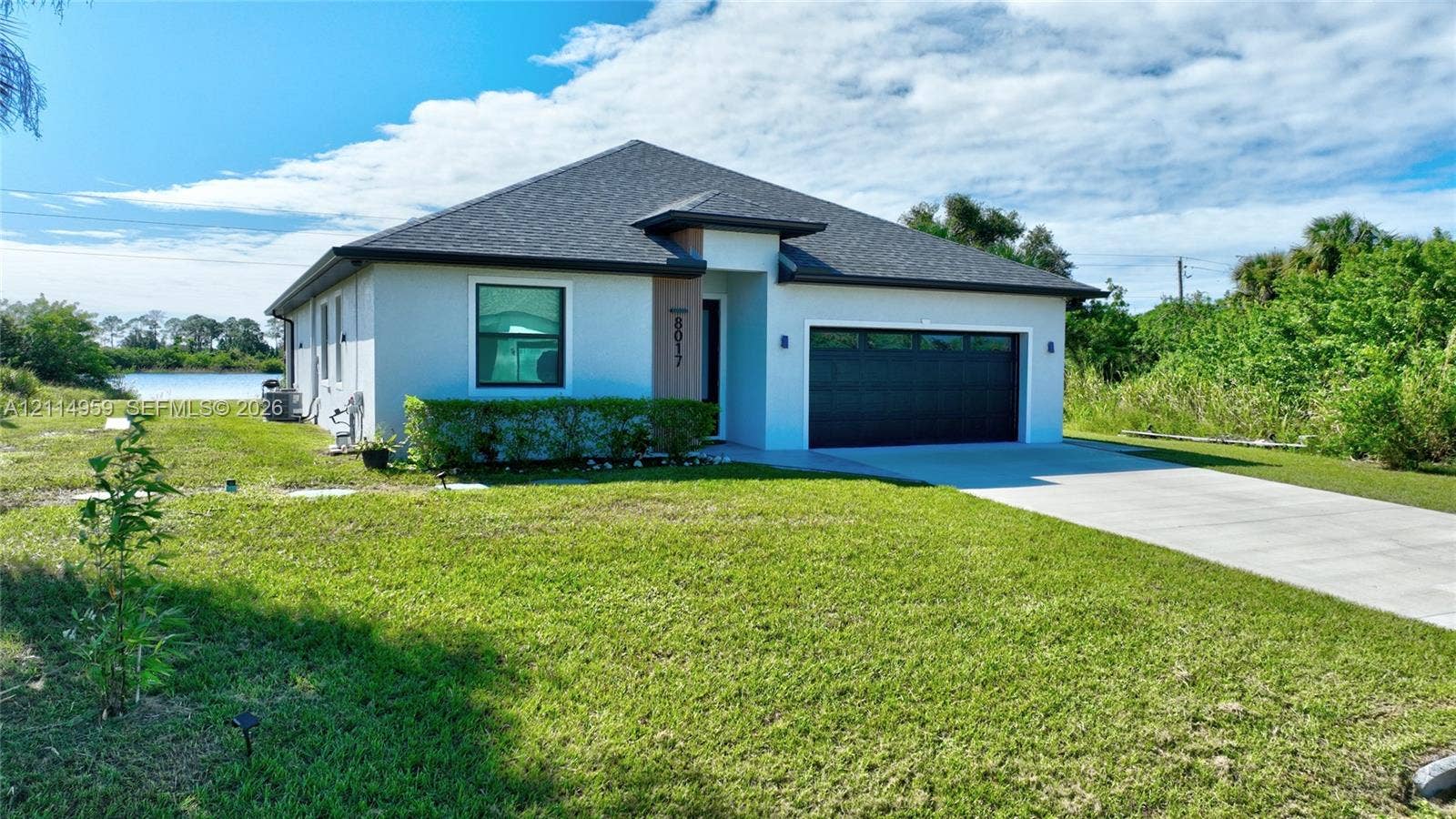 8017 Sunrise Circle, Labelle, FL 33935 Single-story exterior featuring a hip roof, stucco facade, two-car garage with black sectional door, and water frontage