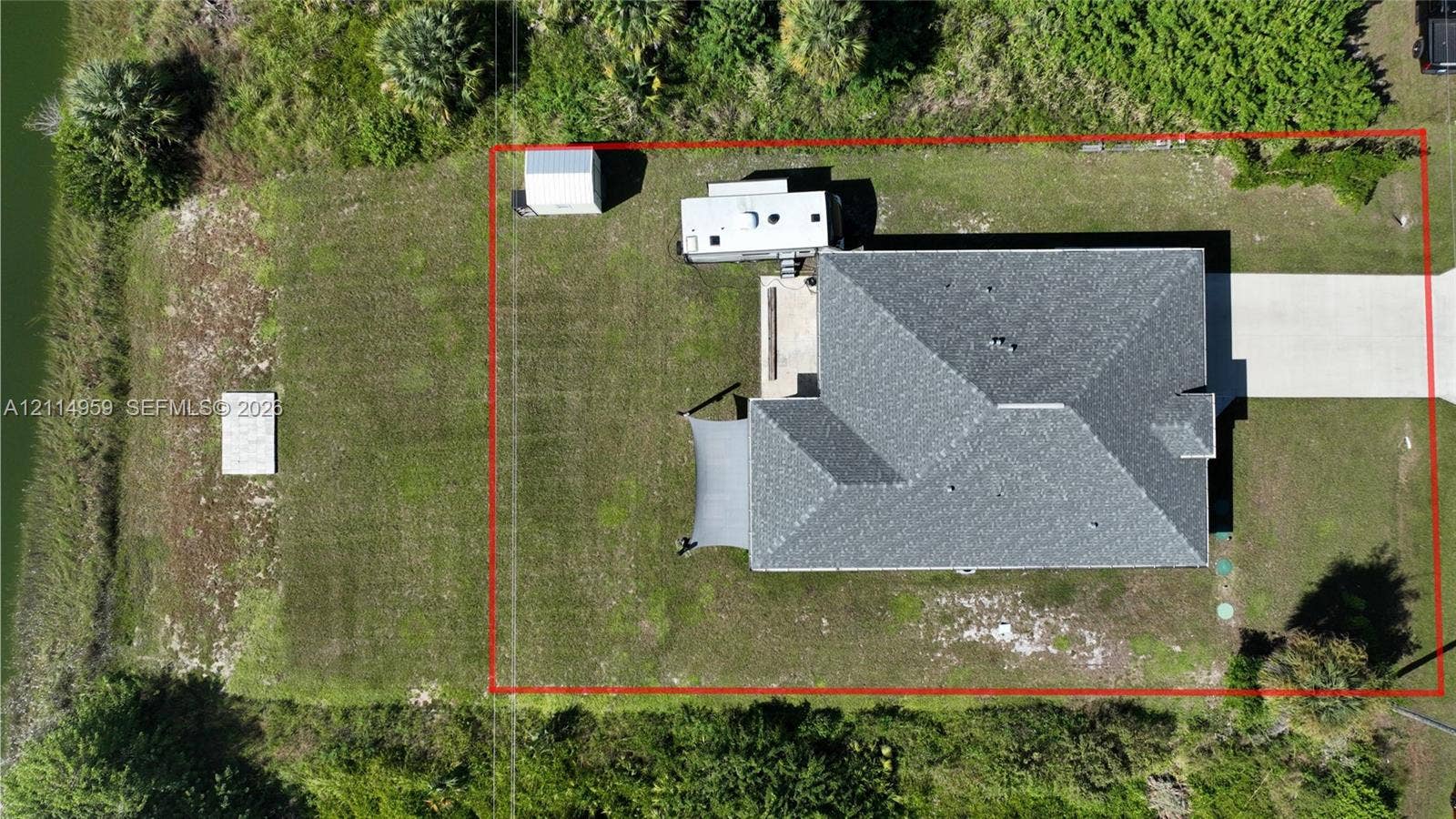 8017 Sunrise Circle, Labelle, FL 33935 Aerial perspective of the property featuring a concrete driveway, multi-faceted roof structure, detached metal storage building, and grass-covered lot
