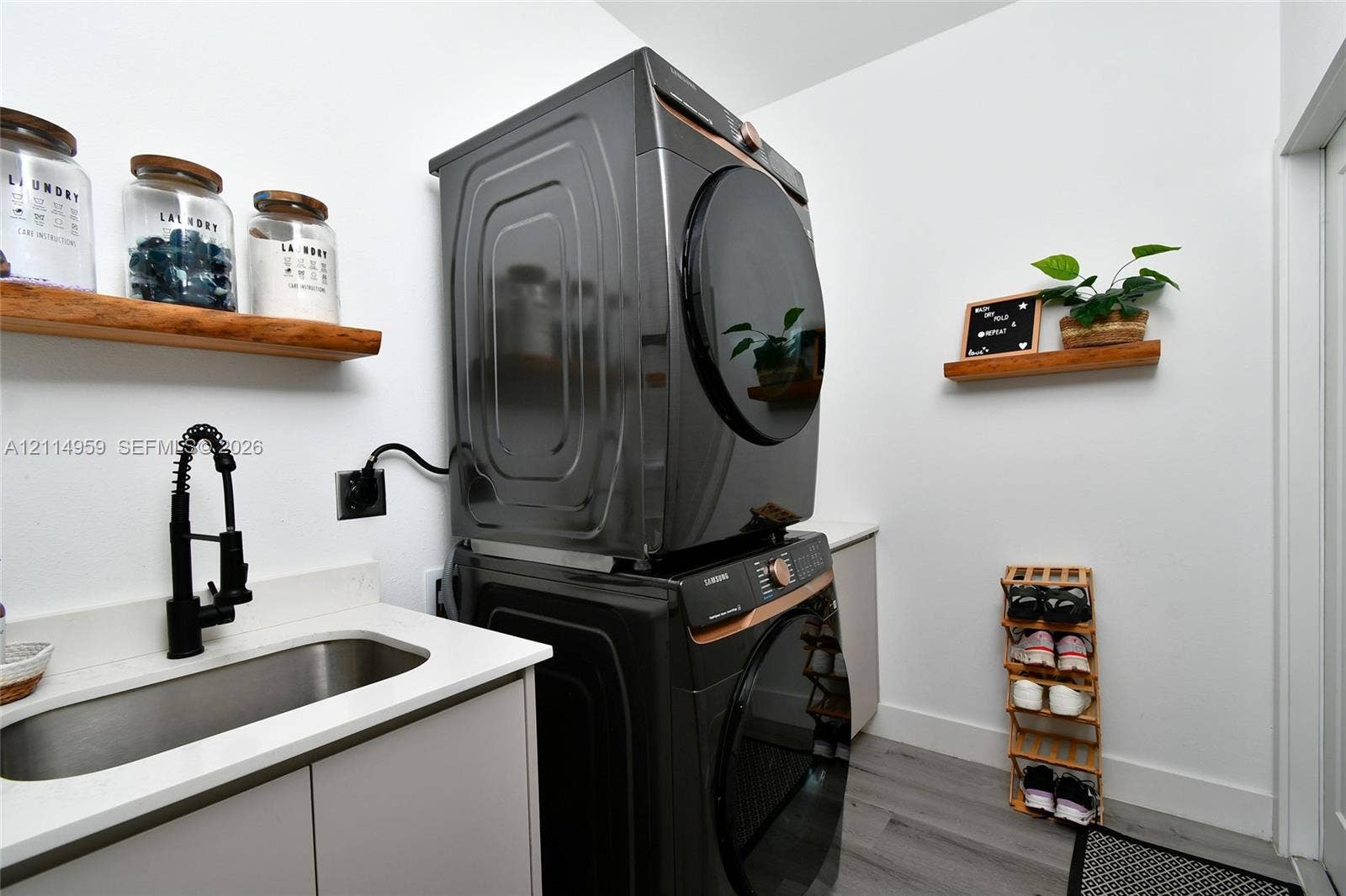 8017 Sunrise Circle, Labelle, FL 33935 Stacked laundry appliances featuring a metallic finish, undermount stainless steel sink, matte black gooseneck faucet, quartz-surfaced countertop, and natural wood-finish wall-mounted shelving