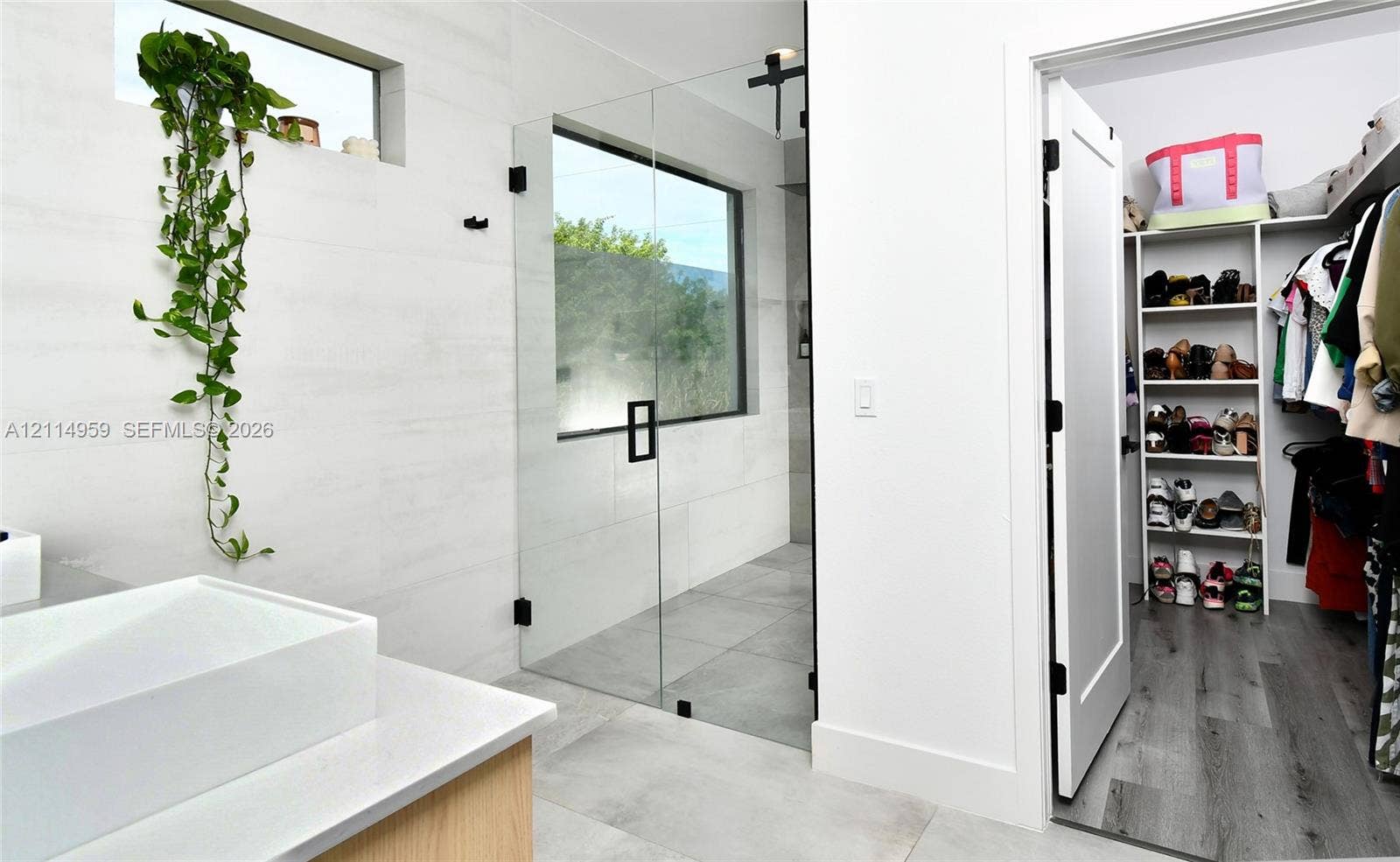 8017 Sunrise Circle, Labelle, FL 33935 Bathroom featuring a frameless glass-enclosed shower with matte black hardware, large-format tile flooring, rectangular vessel sink on a stone-topped vanity, and a walk-in closet with built-in shelving and wood-finish flooring