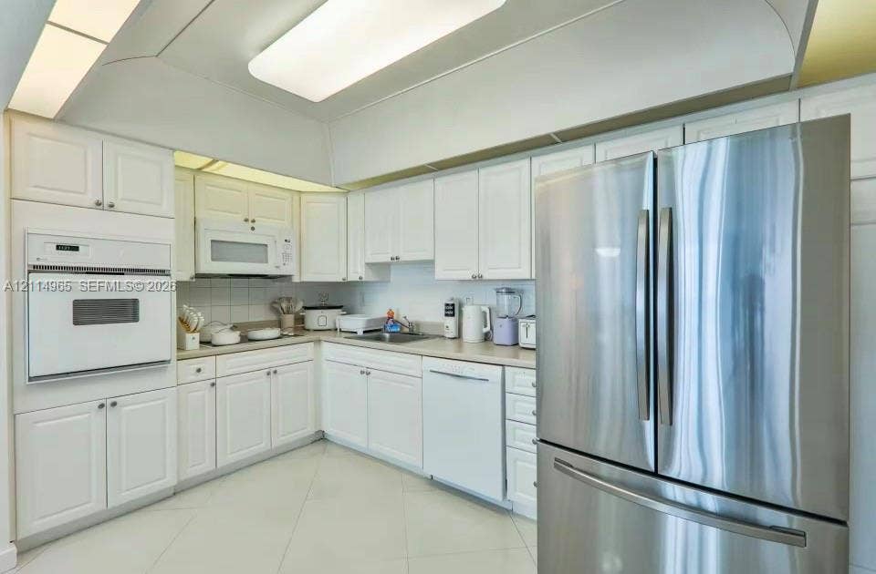 19370 Collins Avenue, #414, Sunny Isles Beach, FL 33160 Kitchen featuring white cabinetry, integrated wall oven, stainless steel refrigerator, neutral solid-surface countertops, and tiled flooring