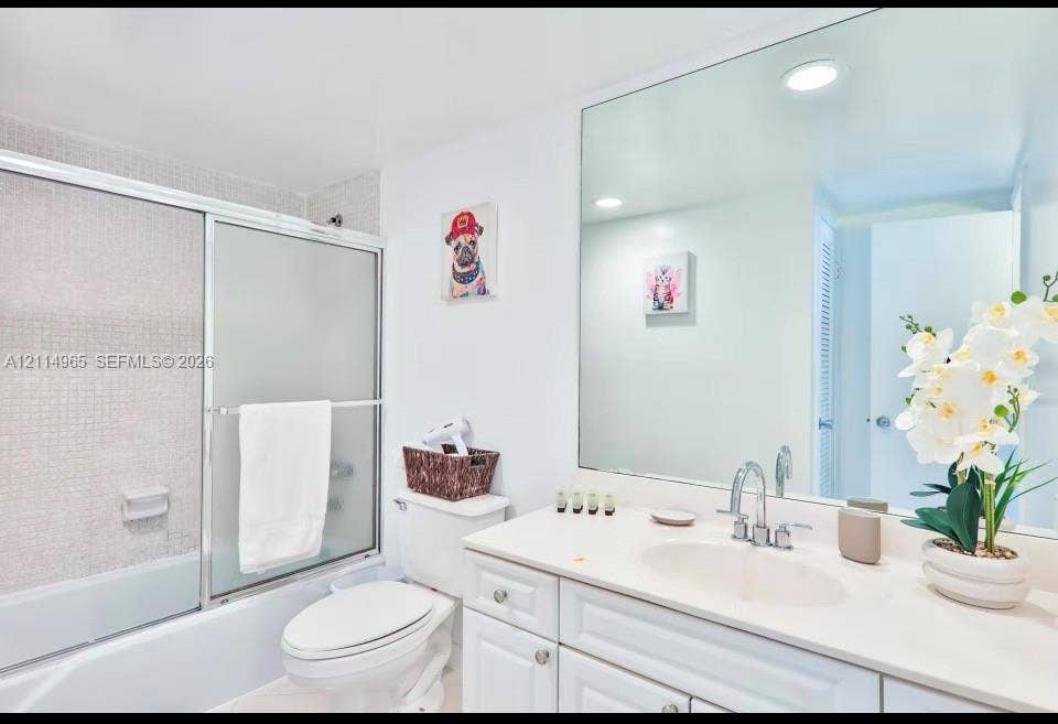 19370 Collins Avenue, #414, Sunny Isles Beach, FL 33160 Bathroom featuring a white vanity with an integrated oval basin, a chrome widespread faucet, a full-width wall mirror, and a shower-tub combination with sliding glass doors and mosaic tile surround