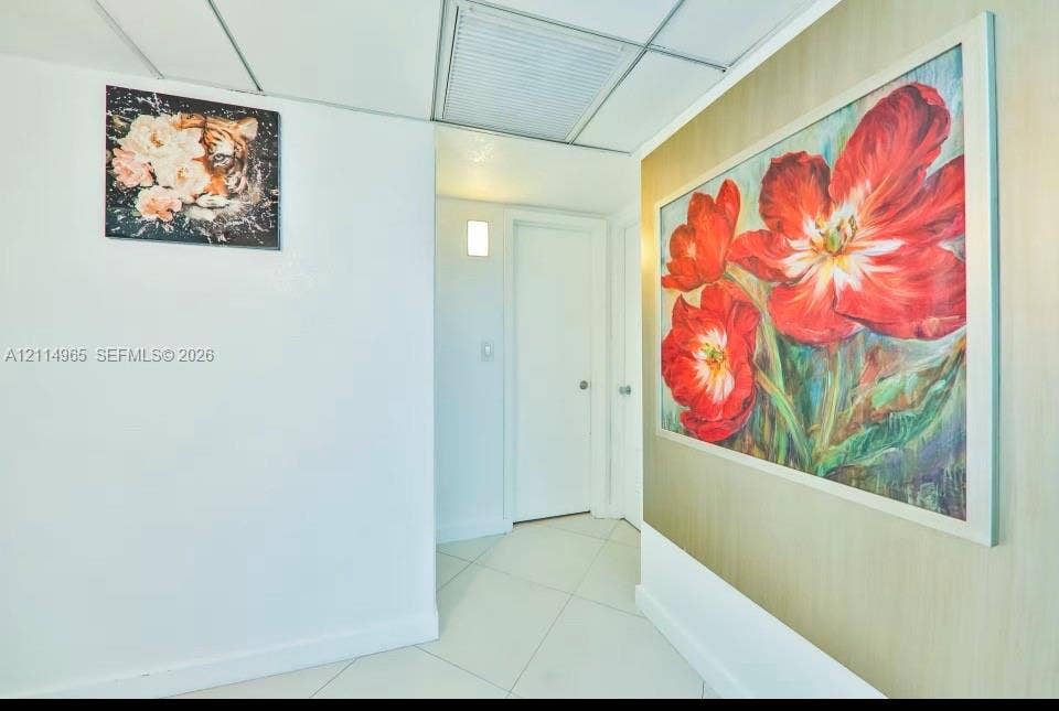 19370 Collins Avenue, #414, Sunny Isles Beach, FL 33160 Interior hallway featuring white tile flooring, neutral wall finishes, a wall-mounted light fixture, and panel doors