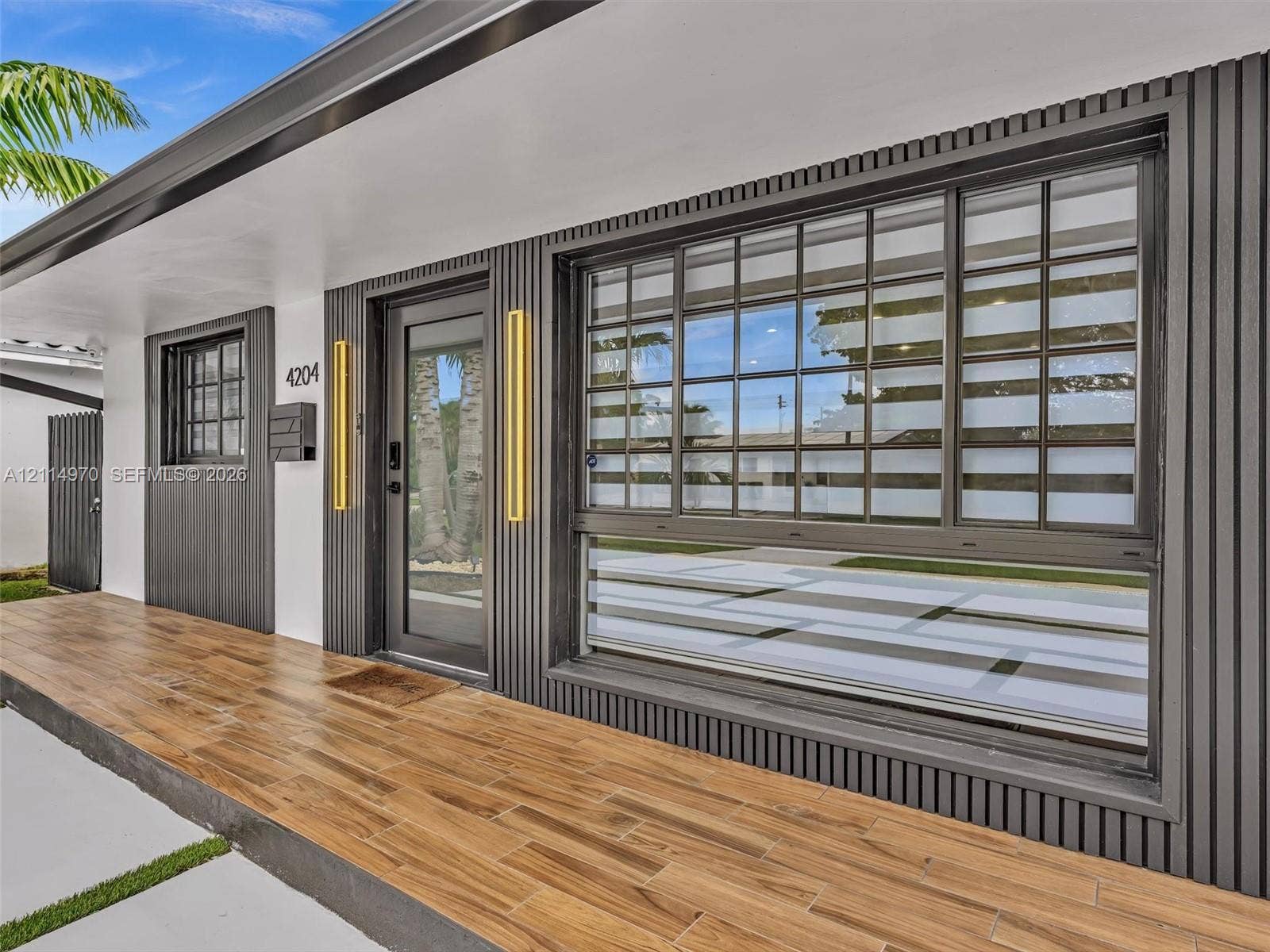 4204 Van Buren Street, Hollywood, Hollywood, FL 33021 Exterior facade featuring vertical slat siding, wood-finish flooring, full-lite glass entry door, grid-patterned windows, and metallic wall-mounted light fixtures