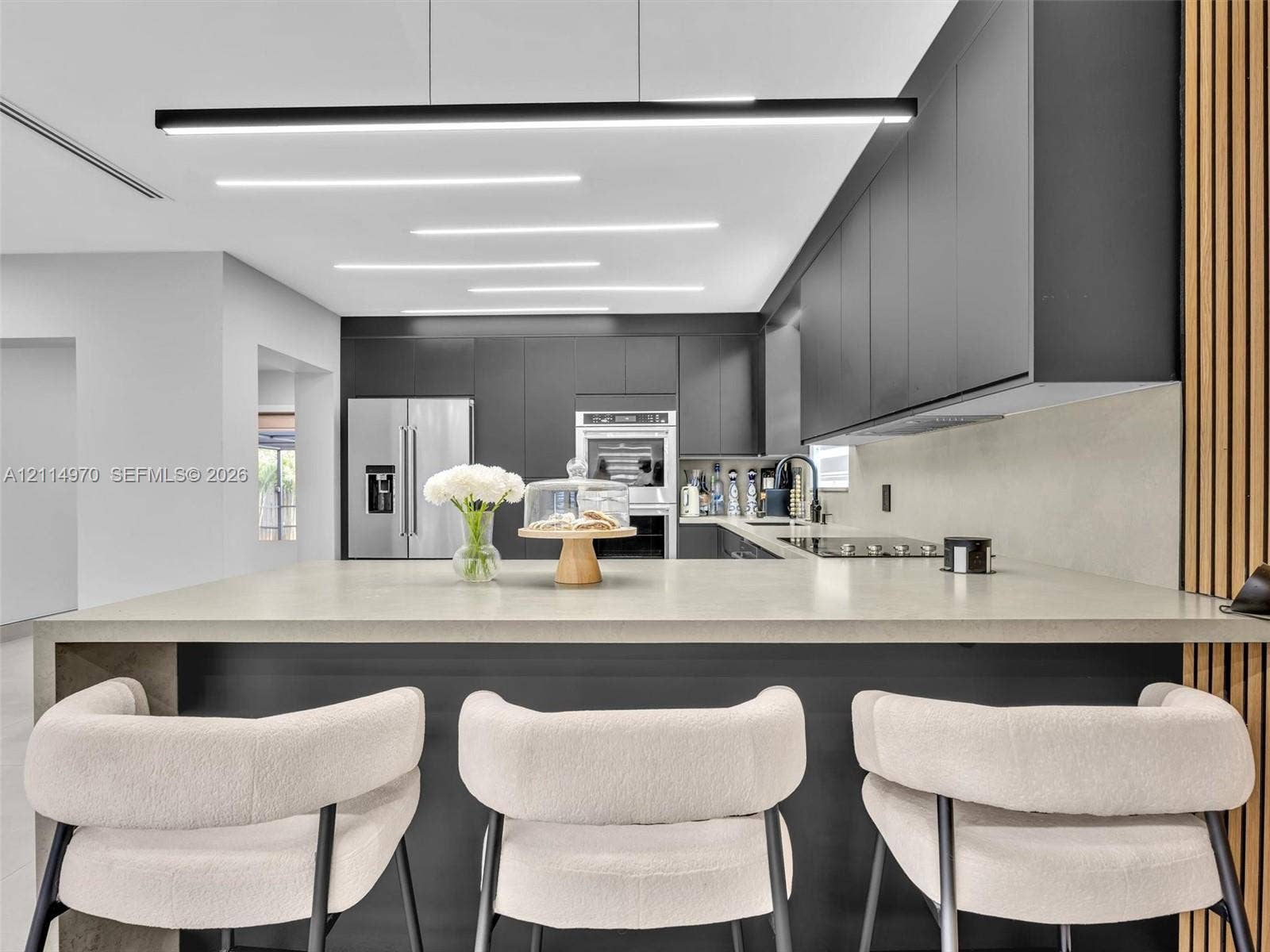 4204 Van Buren Street, Hollywood, Hollywood, FL 33021 Modern kitchen featuring matte charcoal cabinetry, a large waterfall-edge island with a stone-finish countertop, built-in stainless steel appliances, recessed ceiling lighting, and decorative vertical wood-slat wall paneling