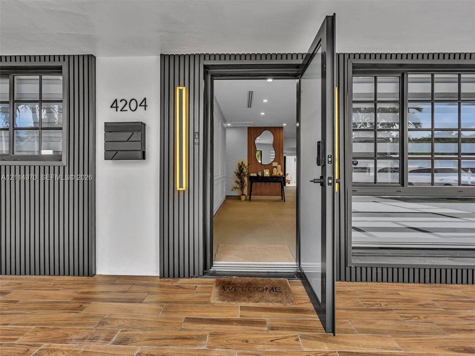 4204 Van Buren Street, Hollywood, Hollywood, FL 33021 Exterior entrance featuring vertical slat siding, wood-finish tile flooring, matte black grid-pane windows, and linear wall-mounted exterior lighting