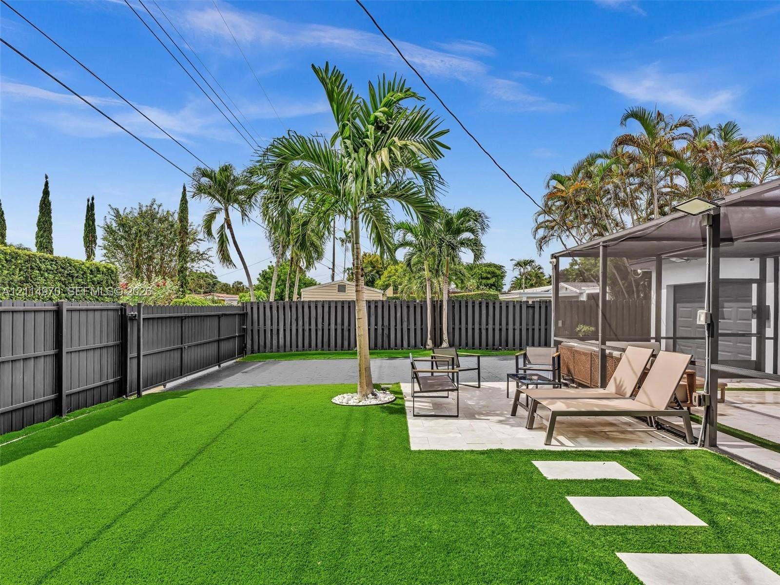 4204 Van Buren Street, Hollywood, Hollywood, FL 33021 Fenced backyard featuring synthetic turf, stone paver pathway, screened-in patio, and mature palm trees