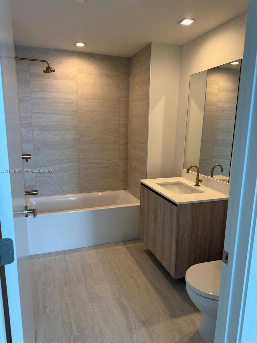 77 SE 5th Street, #2406, Miami, FL 33131 Bathroom featuring a floating vanity with wood-finish cabinetry, a white countertop with an integrated sink, a rectangular wall-mounted mirror, floor-to-ceiling large-format tile surround, and metallic fixtures