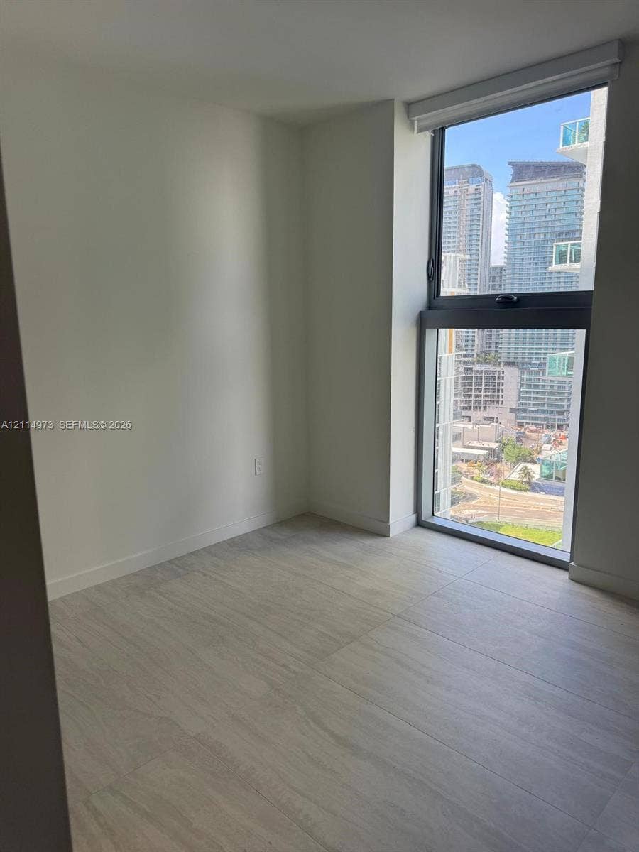 77 SE 5th Street, #2406, Miami, FL 33131 Neutral interior space featuring large-format tile flooring, floor-to-ceiling windows, and urban cityscape backdrop