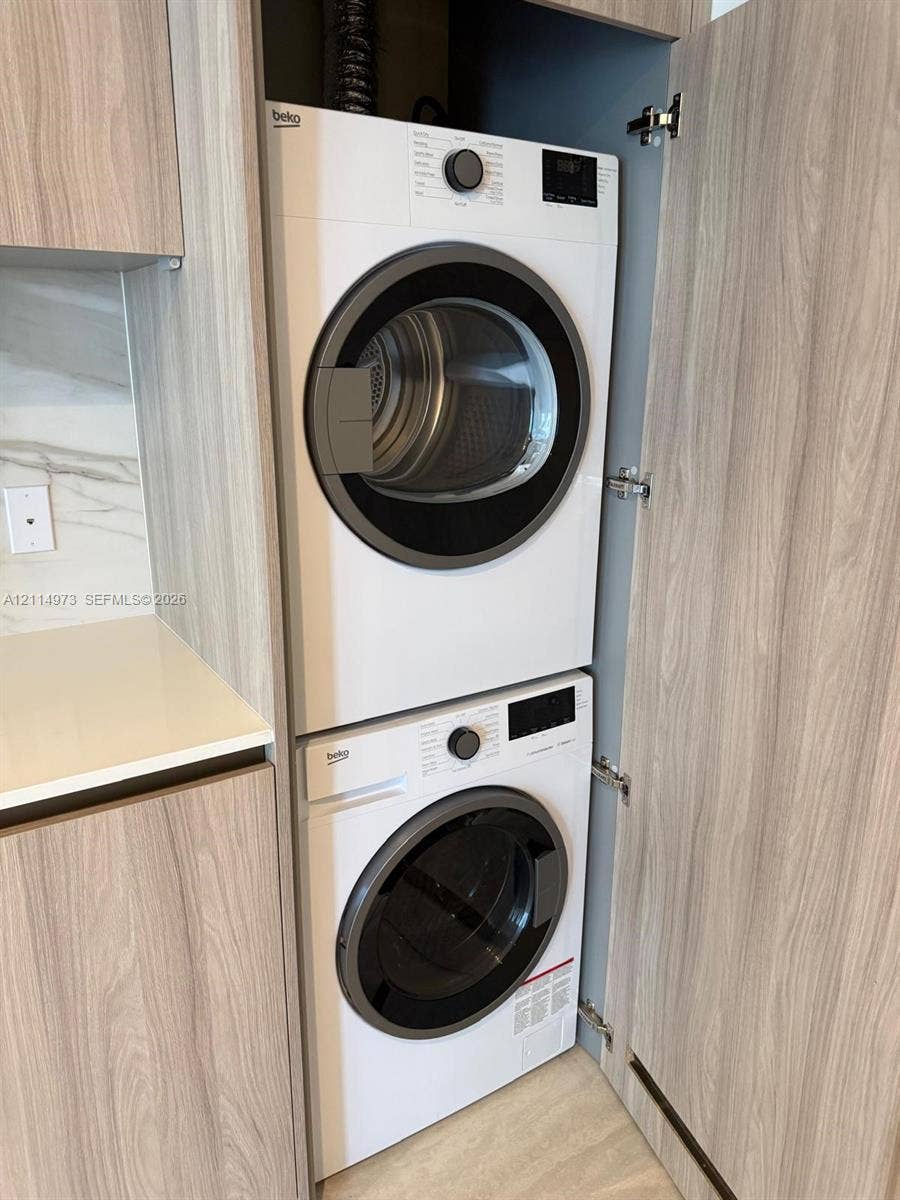 77 SE 5th Street, #2406, Miami, FL 33131 Built-in stacked laundry unit with light-toned wood-finish cabinetry, quartz countertop, and stone-finish backsplash