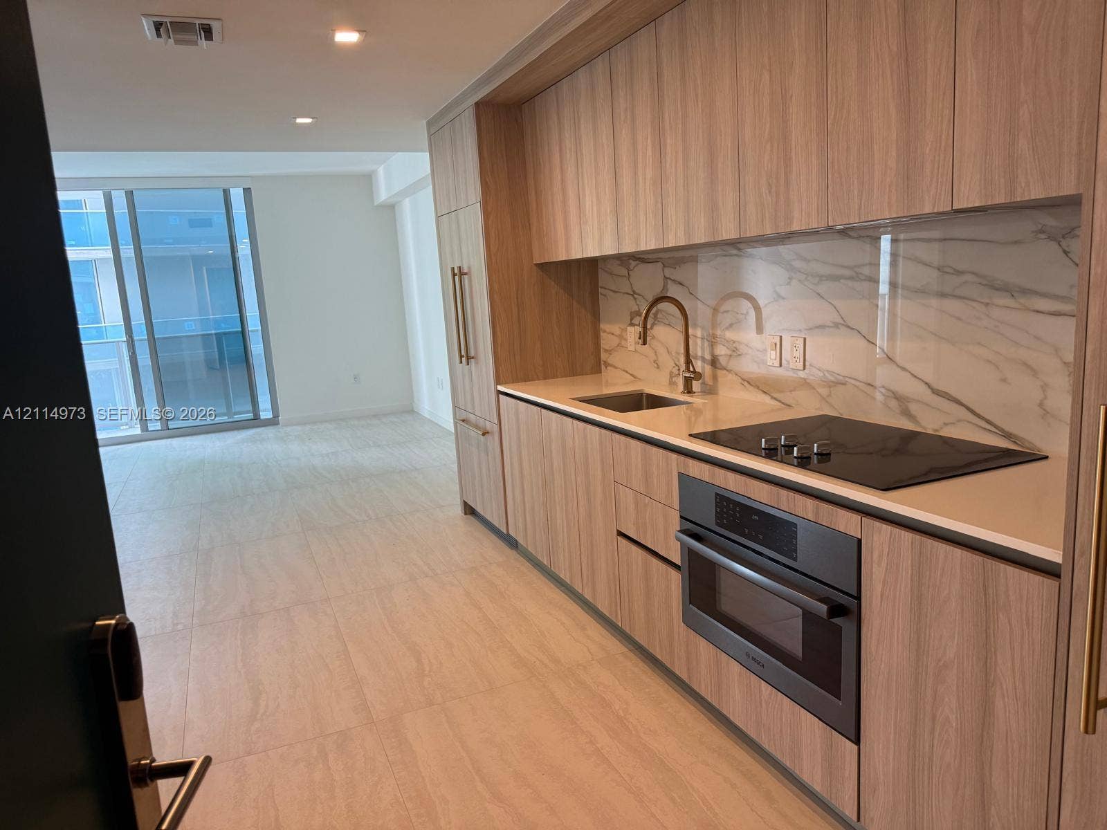 77 SE 5th Street, #2406, Miami, FL 33131 Kitchen featuring flat-panel wood-finish cabinetry, integrated appliances, light-toned stone-patterned backsplash, and ceramic tile flooring