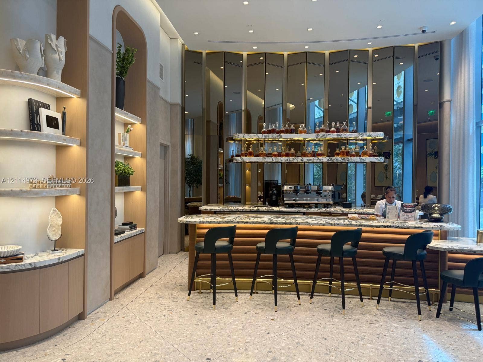 77 SE 5th Street, #2406, Miami, FL 33131 Bar area featuring a stone-topped counter, reeded wood-finish base, integrated lighting, stone shelving, and a mirrored paneled wall