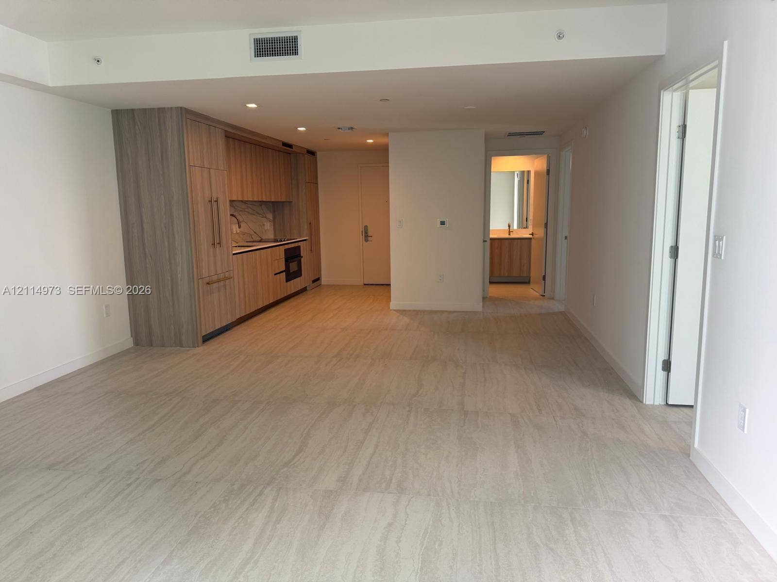 77 SE 5th Street, #2406, Miami, FL 33131 Open-plan living area featuring wood-finish cabinetry, stone-patterned backsplash, recessed lighting, and tile flooring