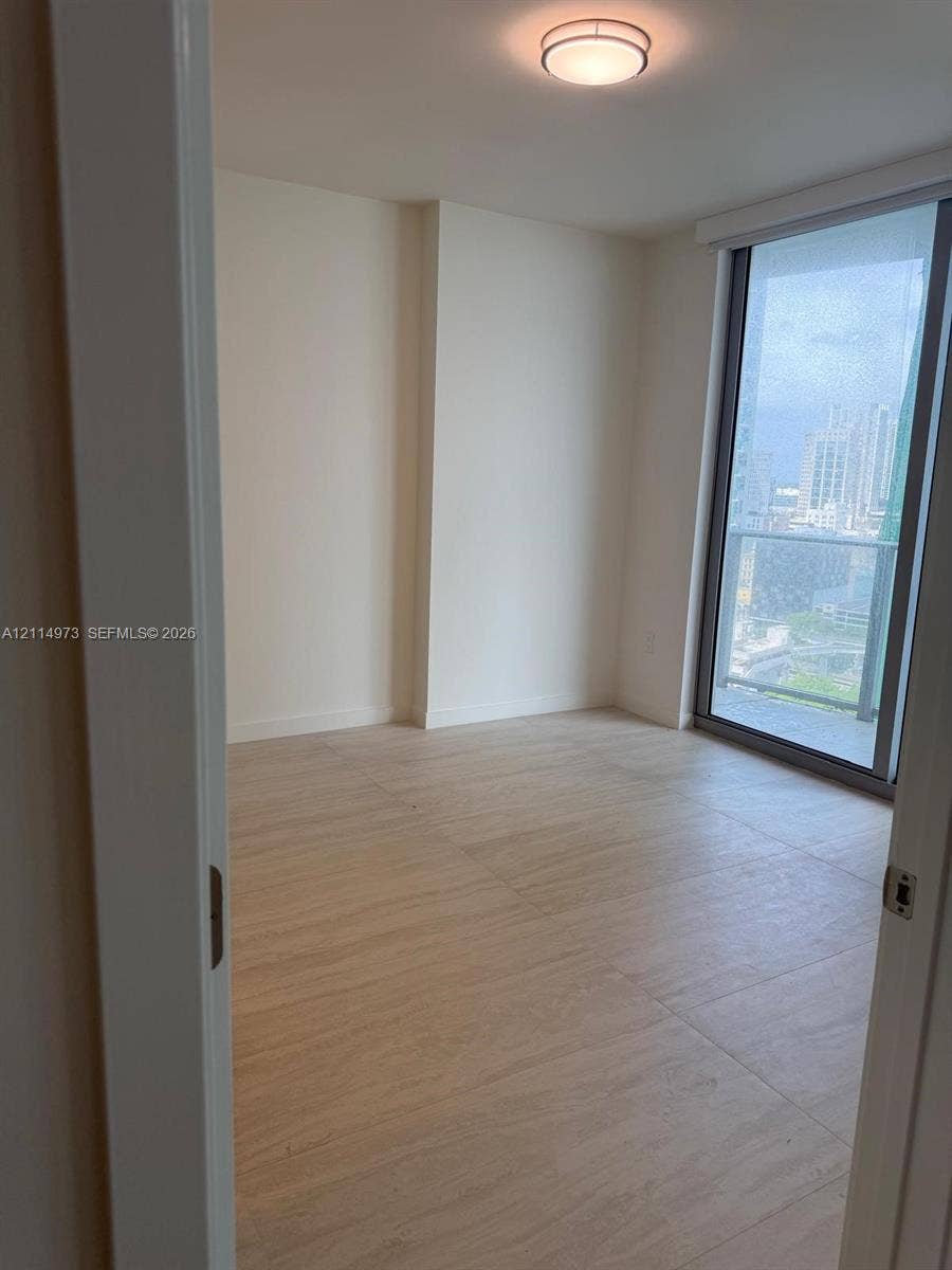 77 SE 5th Street, #2406, Miami, FL 33131 Neutral-toned interior featuring wood-finish flooring, floor-to-ceiling glass sliding door, integrated balcony, and flush-mount circular lighting fixture