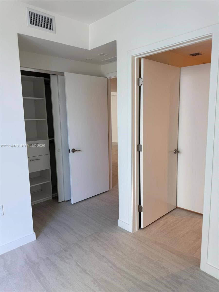 77 SE 5th Street, #2406, Miami, FL 33131 Interior space featuring wood-finish flooring, white solid-core doors with brushed nickel hardware, and built-in closet storage with integrated shelving and drawers