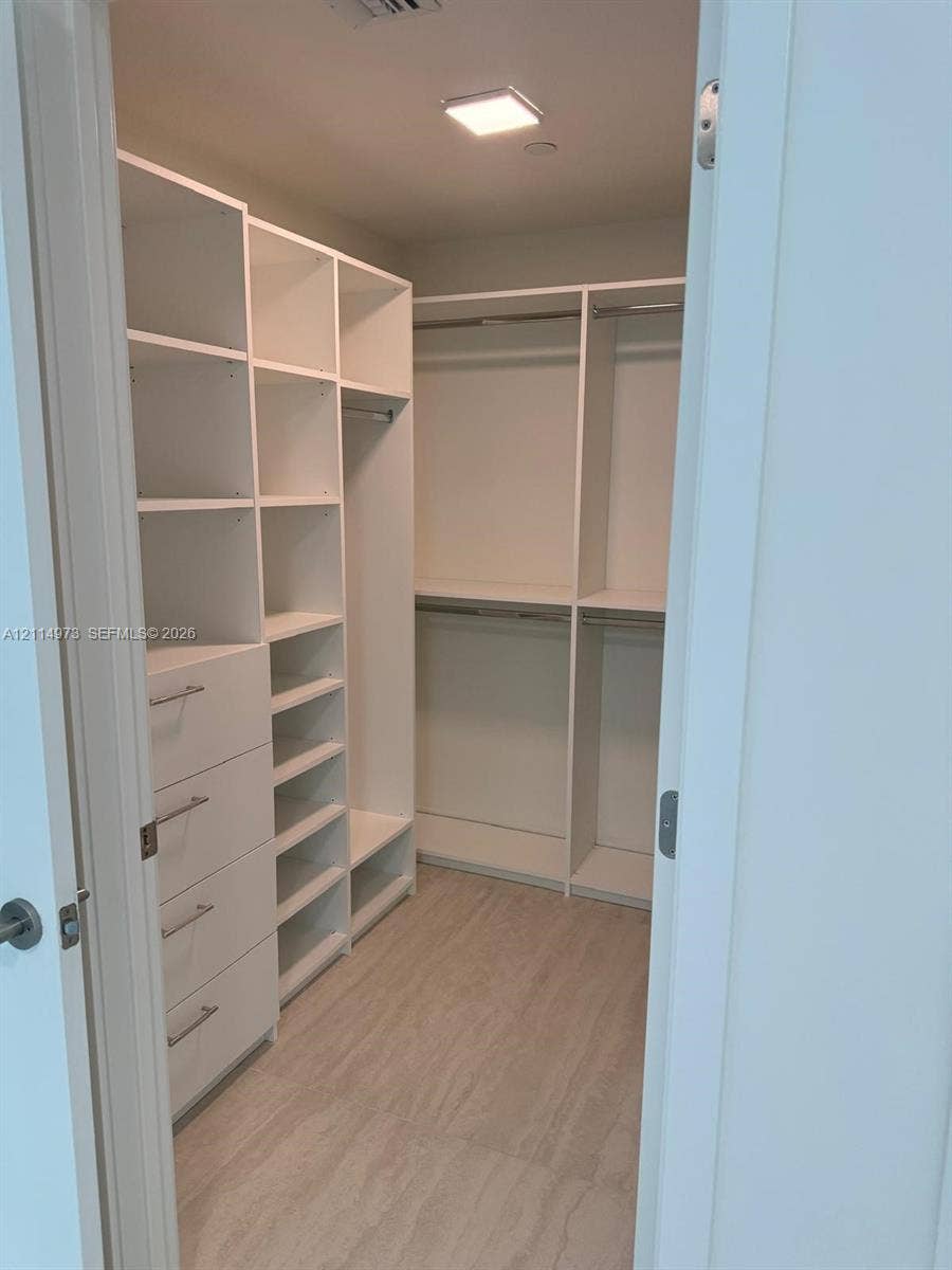 77 SE 5th Street, #2406, Miami, FL 33131 Walk-in closet featuring white built-in shelving, integrated dresser drawers with metal hardware, double-tier hanging rods, and wood-finish flooring