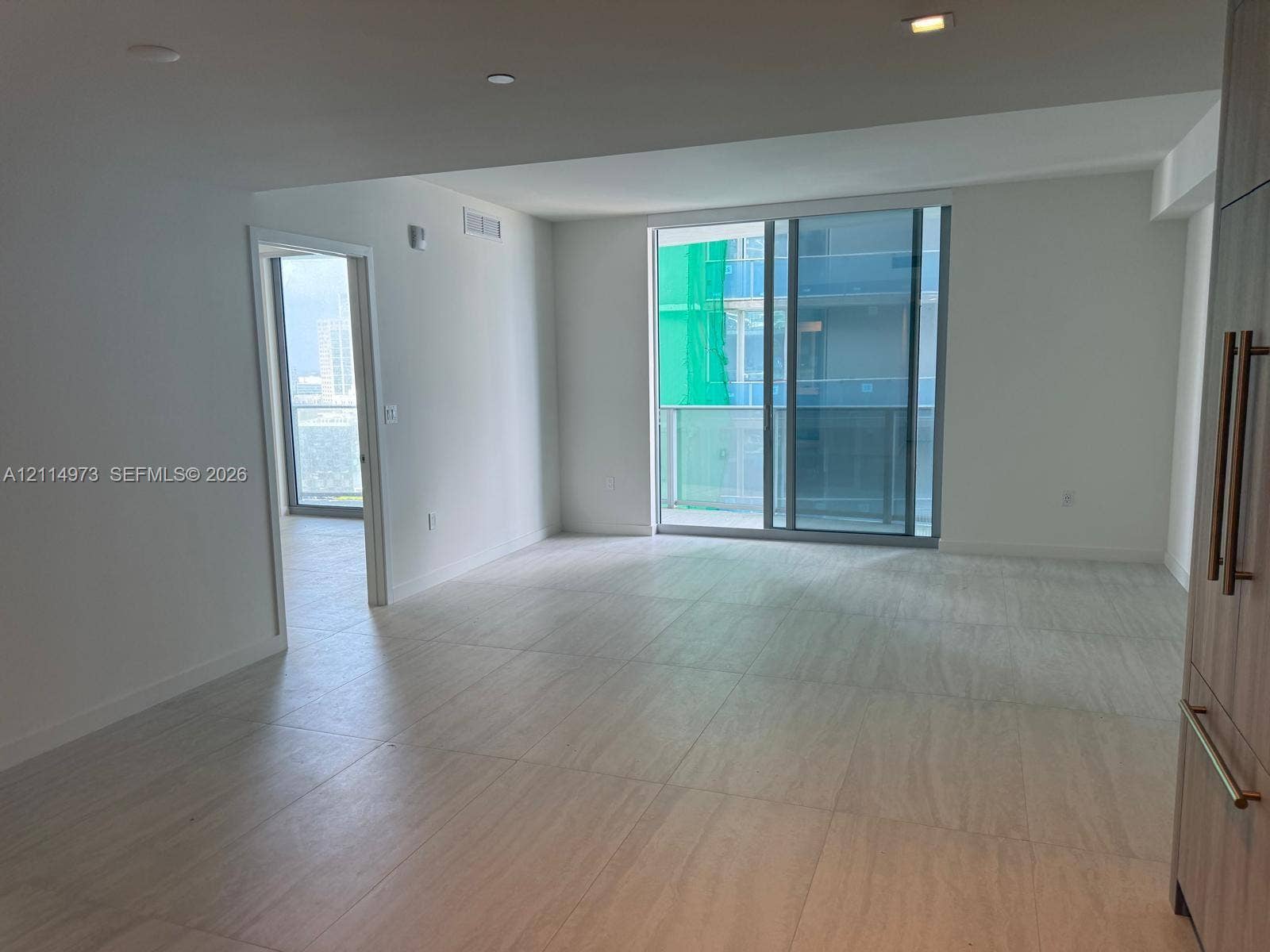 77 SE 5th Street, #2406, Miami, FL 33131 Open-concept living space featuring neutral large-format tile flooring, floor-to-ceiling sliding glass doors, built-in cabinetry with metallic pulls, and recessed lighting