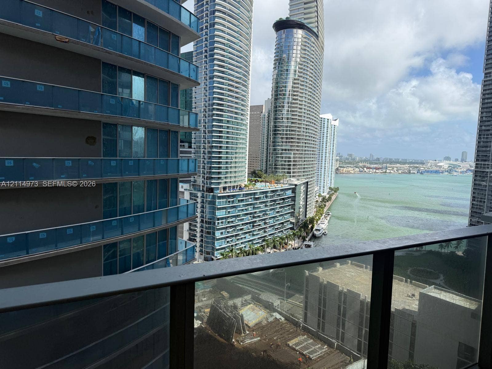77 SE 5th Street, #2406, Miami, FL 33131 Balcony featuring metal railings with glass panels overlooking a bay, high-rise urban structures, and waterfront scenery