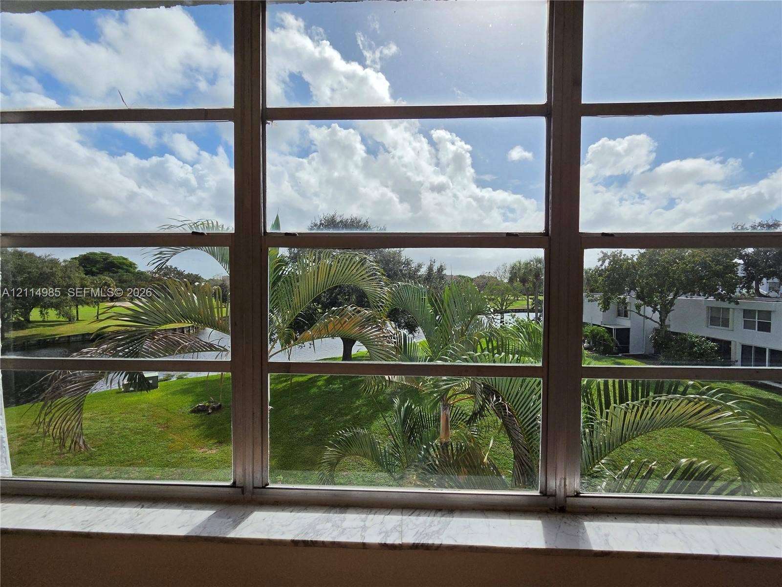 9441 Live Oak Place, #308, Davie, Davie, FL 33324 Multi-pane horizontal window featuring a natural stone sill, framing exterior water frontage, mature palm trees, and manicured green space