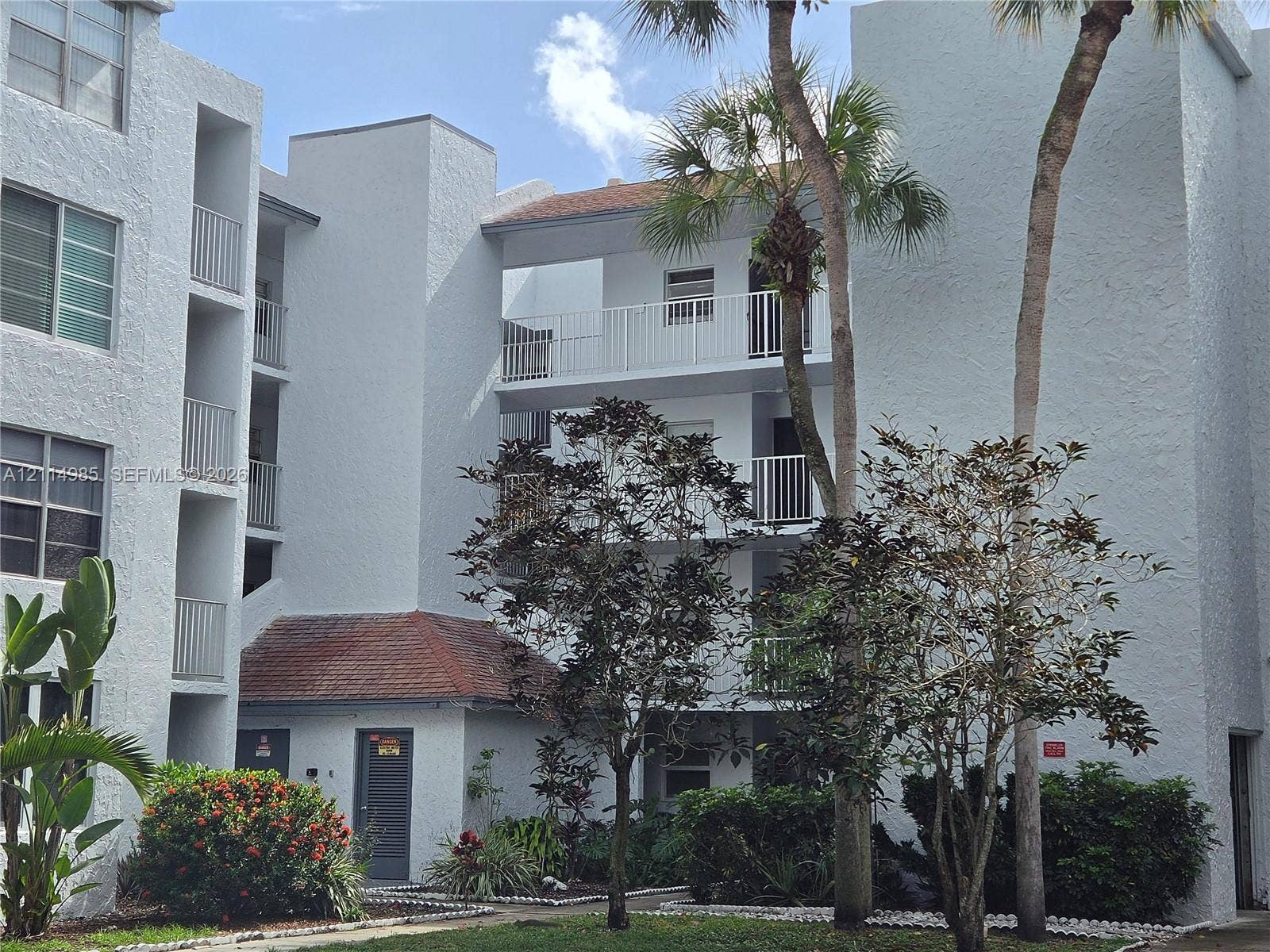 9441 Live Oak Place, #308, Davie, Davie, FL 33324 Multi-story residential building exterior featuring a textured stucco facade, tiered balconies with white railings, and integrated landscaping with mature palm trees