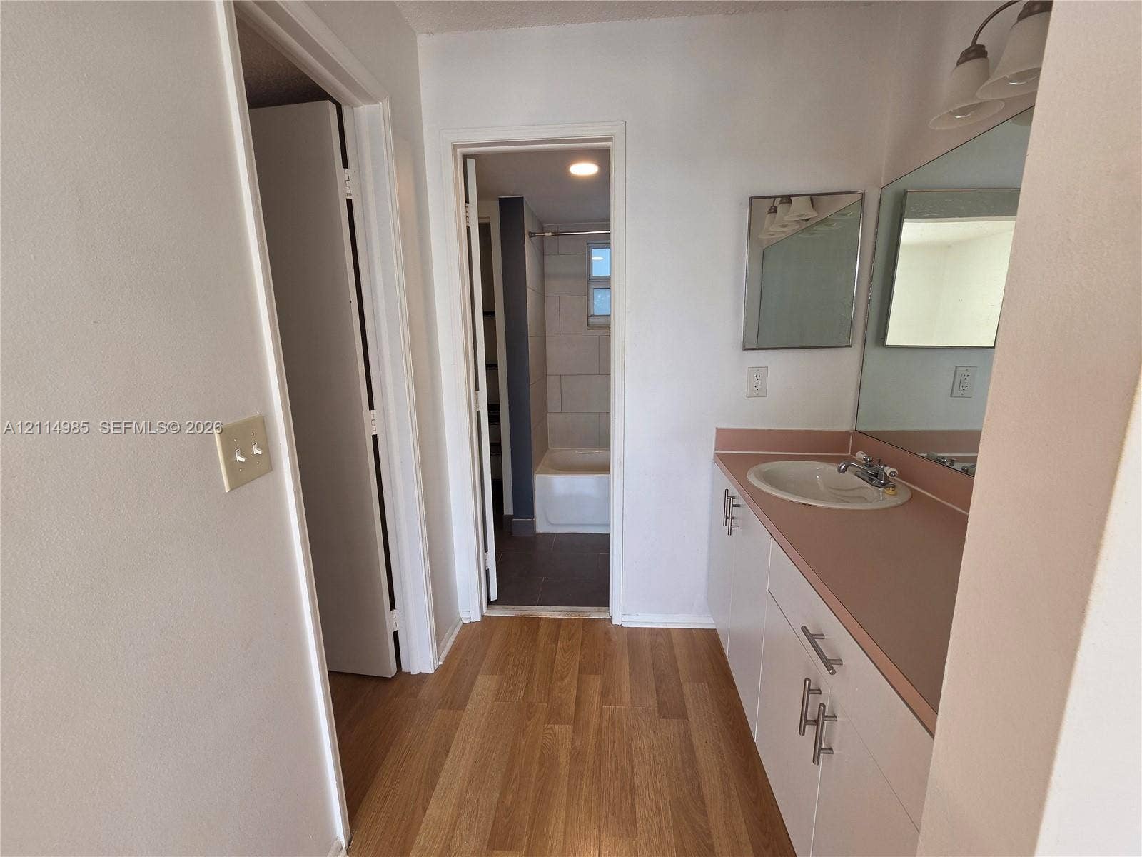 9441 Live Oak Place, #308, Davie, Davie, FL 33324 Bathroom featuring wood-finish flooring, a white vanity with a solid-surface countertop and integrated sink, a full-width wall mirror, and a tiled shower enclosure