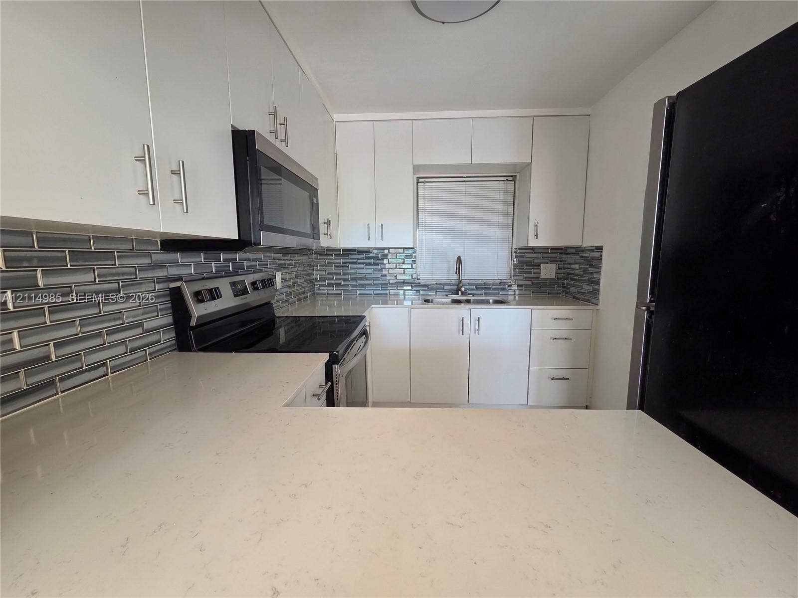 9441 Live Oak Place, #308, Davie, Davie, FL 33324 Kitchen featuring white flat-panel cabinetry, light-toned stone-surface countertops, subway tile backsplash, stainless steel appliances, and a double-basin undermount sink