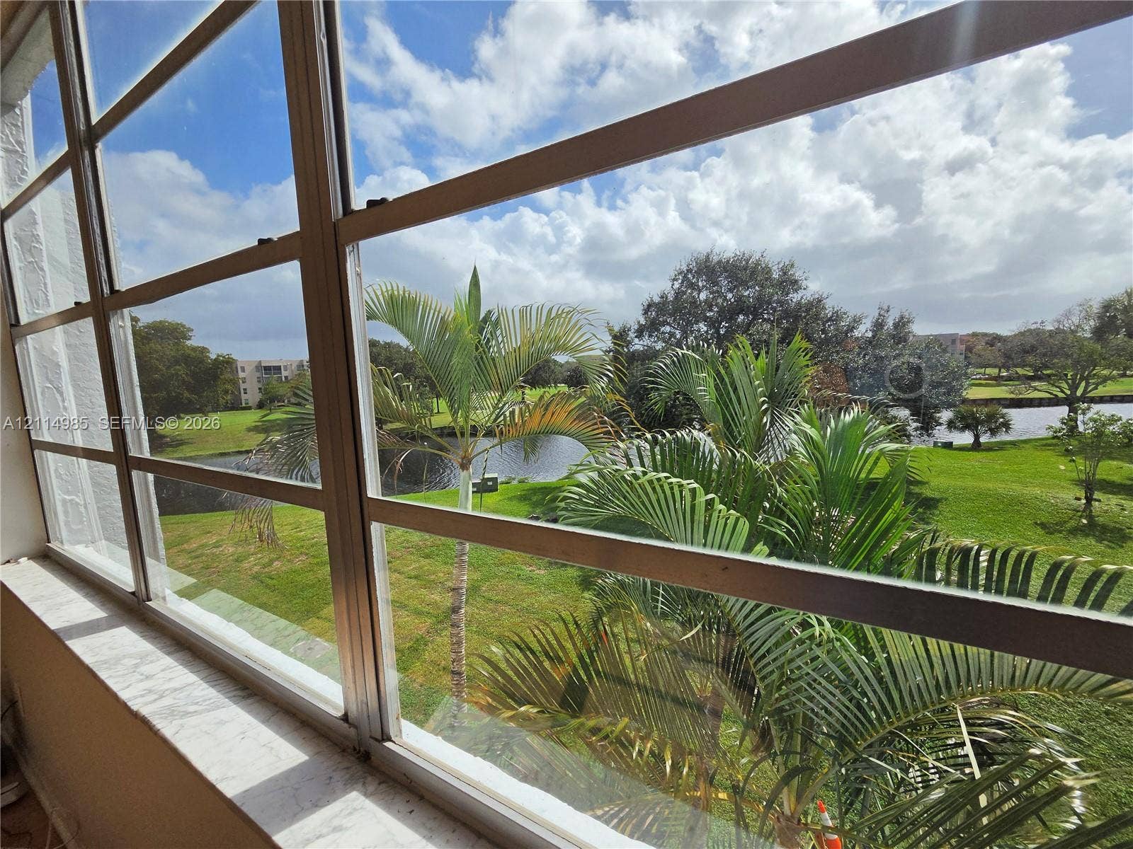 9441 Live Oak Place, #308, Davie, Davie, FL 33324 Multi-pane window featuring a smooth-finish sill, showcasing exterior water frontage, mature palm trees, and manicured green space