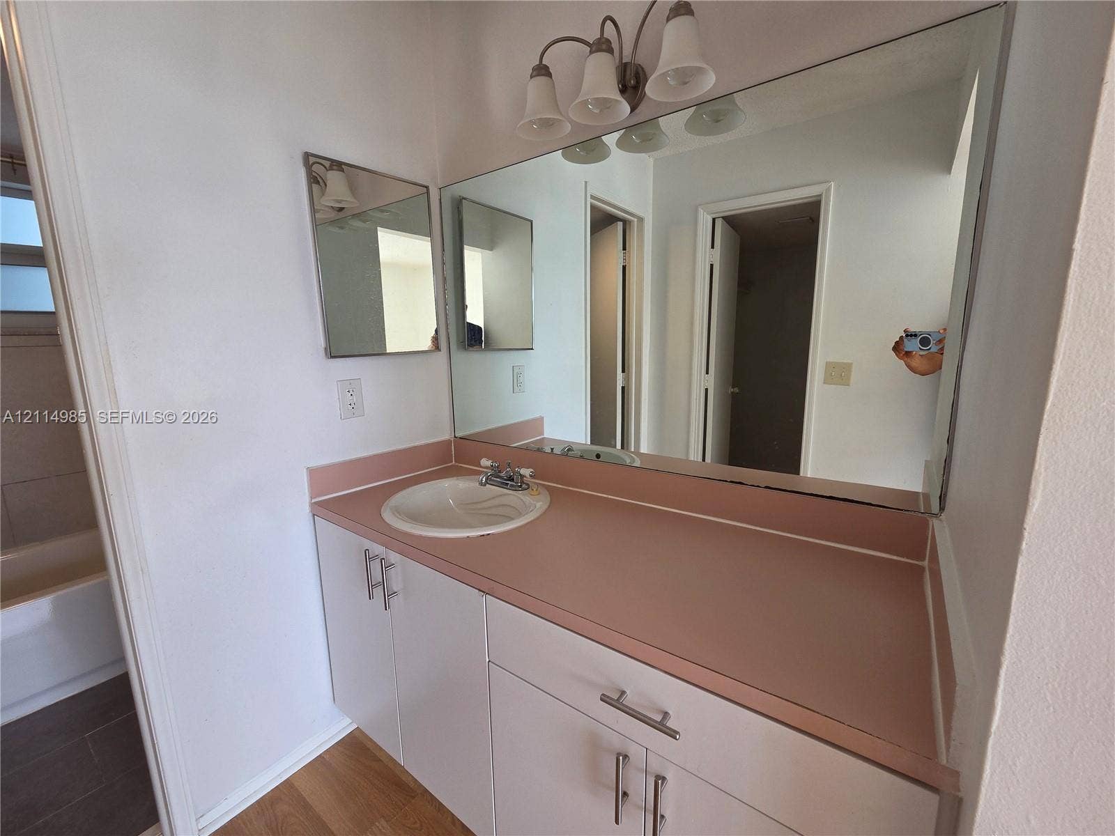 9441 Live Oak Place, #308, Davie, Davie, FL 33324 Bathroom vanity featuring a solid-surface countertop, integrated basin, white cabinetry with brushed-metal hardware, and a large-format vanity mirror with a three-light fixture