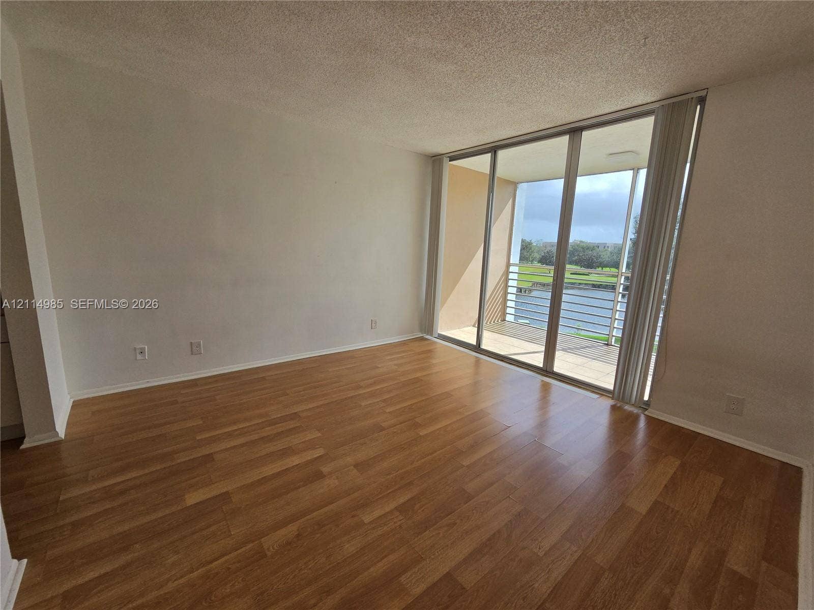9441 Live Oak Place, #308, Davie, Davie, FL 33324 Wood-finish flooring, sliding glass patio doors, and a covered balcony overlooking a water feature