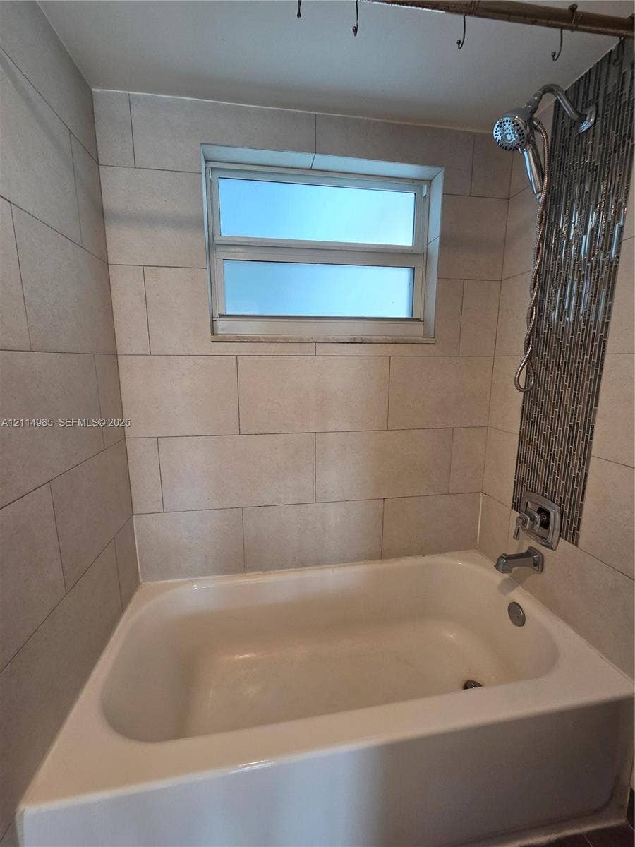 9441 Live Oak Place, #308, Davie, Davie, FL 33324 Bathtub enclosure featuring large-format neutral wall tile, a vertical decorative glass mosaic tile accent strip, and a chrome hand-held shower fixture