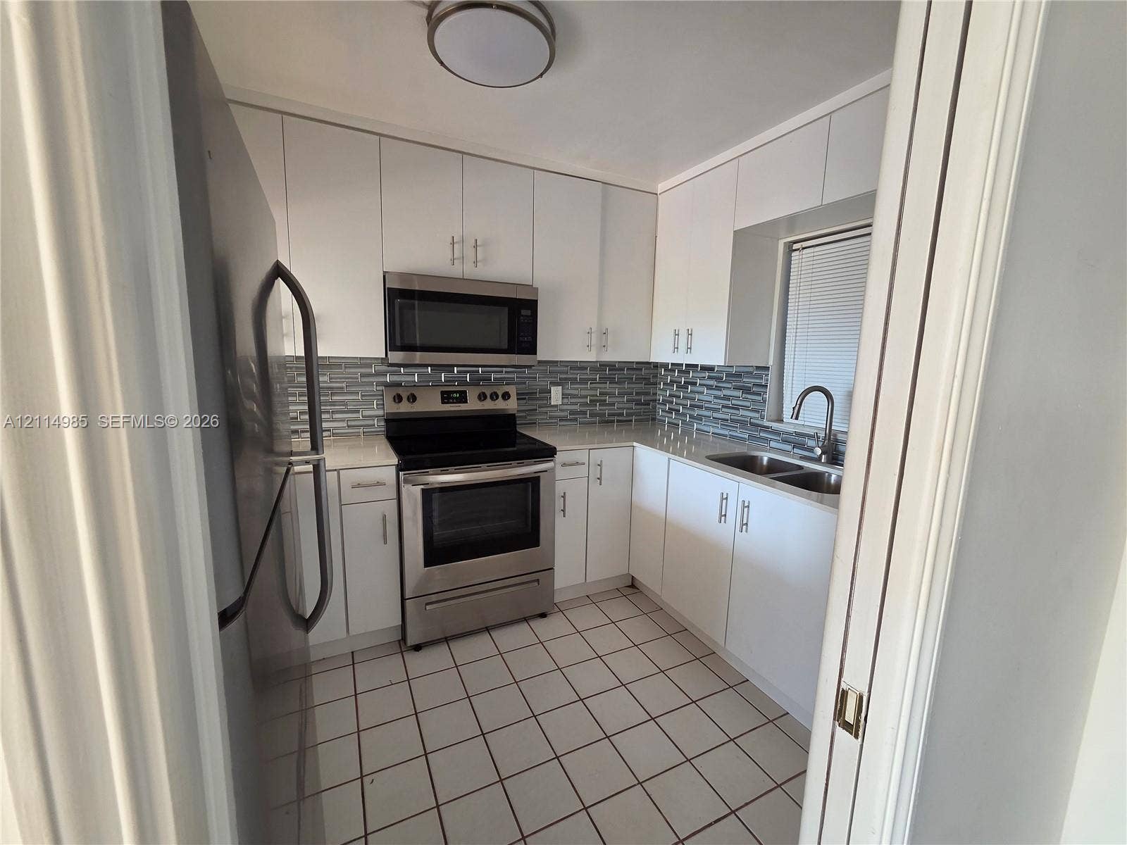 9441 Live Oak Place, #308, Davie, Davie, FL 33324 Kitchen featuring stainless steel appliances, white cabinetry, light-toned countertops, multi-toned tile backsplash, and square floor tiling
