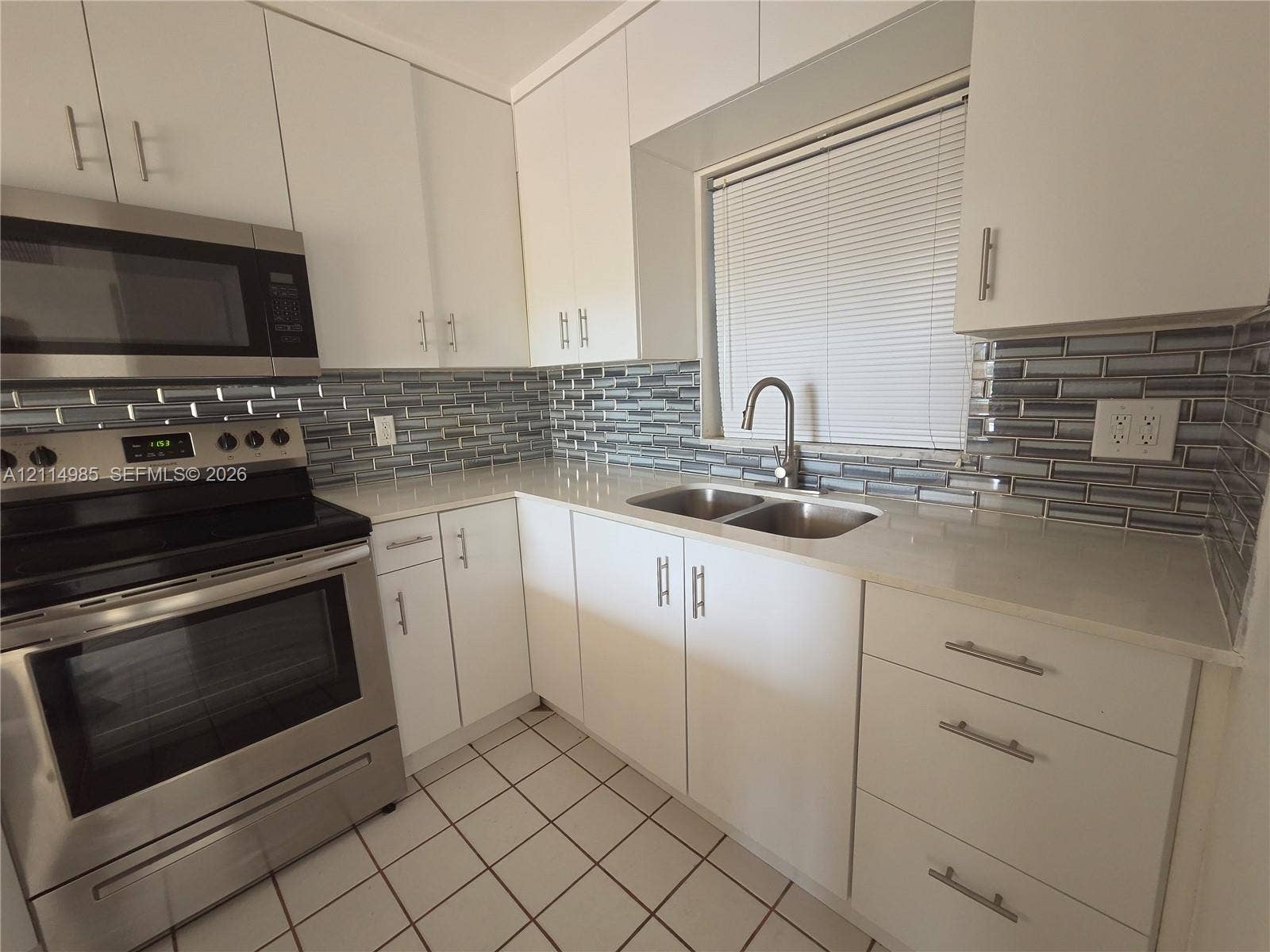 9441 Live Oak Place, #308, Davie, Davie, FL 33324 Kitchen featuring white flat-panel cabinetry, stainless steel appliances, light-toned stone countertops, a multi-tonal glass tile backsplash, and dual-basin sink with a gooseneck faucet