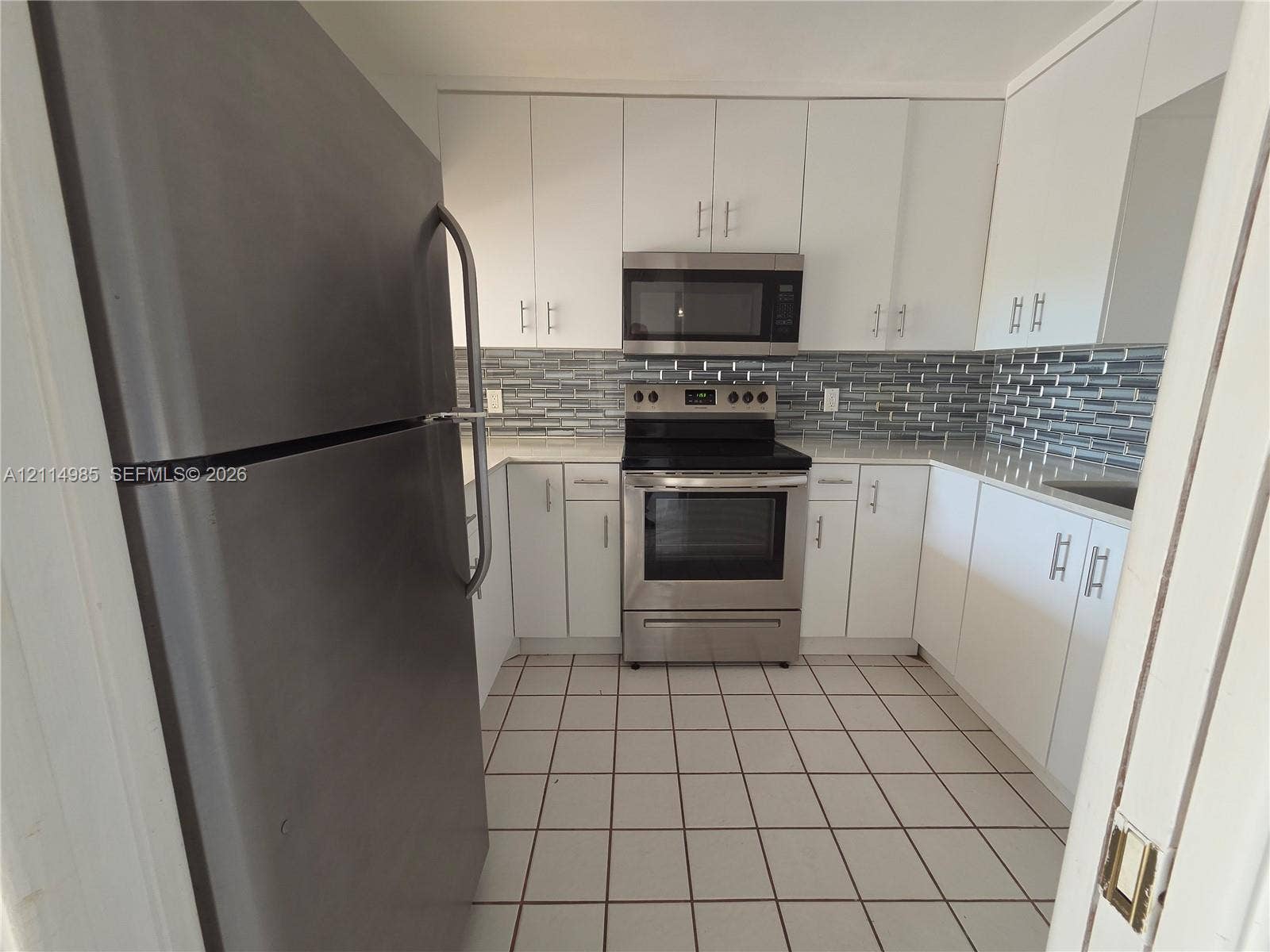 9441 Live Oak Place, #308, Davie, Davie, FL 33324 Kitchen featuring white shaker-style cabinetry, stainless steel appliances, patterned glass tile backsplash, stone-surface countertops, and tiled flooring