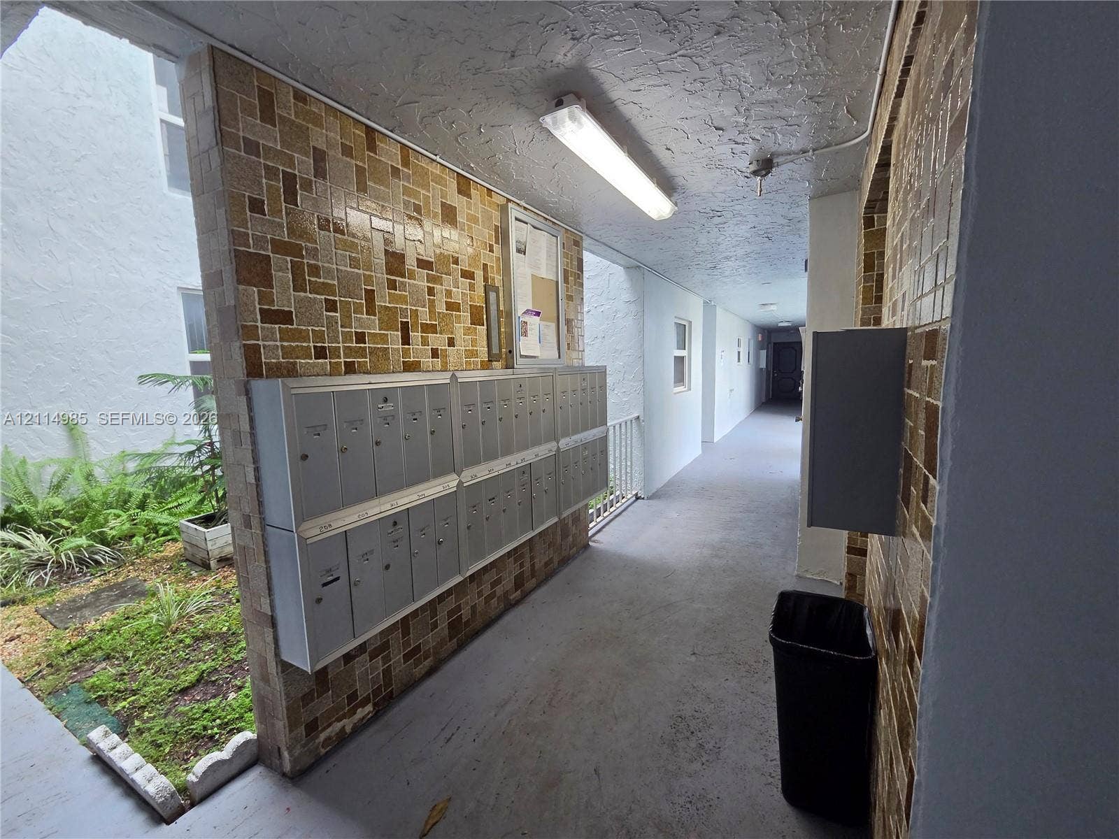 9441 Live Oak Place, #308, Davie, Davie, FL 33324 Covered outdoor corridor featuring textured tile wall cladding, integrated stainless steel mailbox bank, and linear overhead lighting