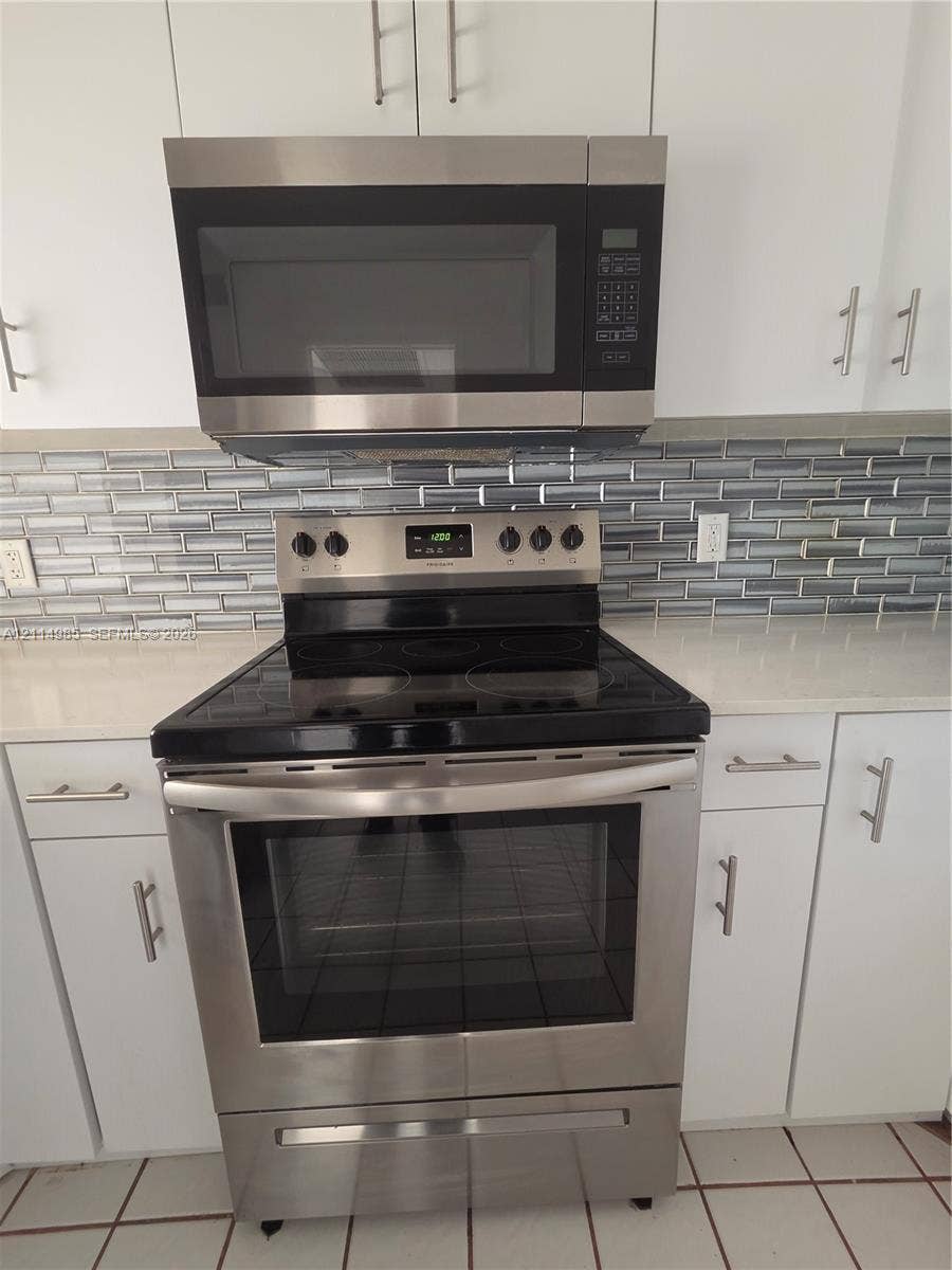 9441 Live Oak Place, #308, Davie, Davie, FL 33324 Stainless steel electric range and microwave, white cabinetry, light-toned countertop, and glass tile backsplash