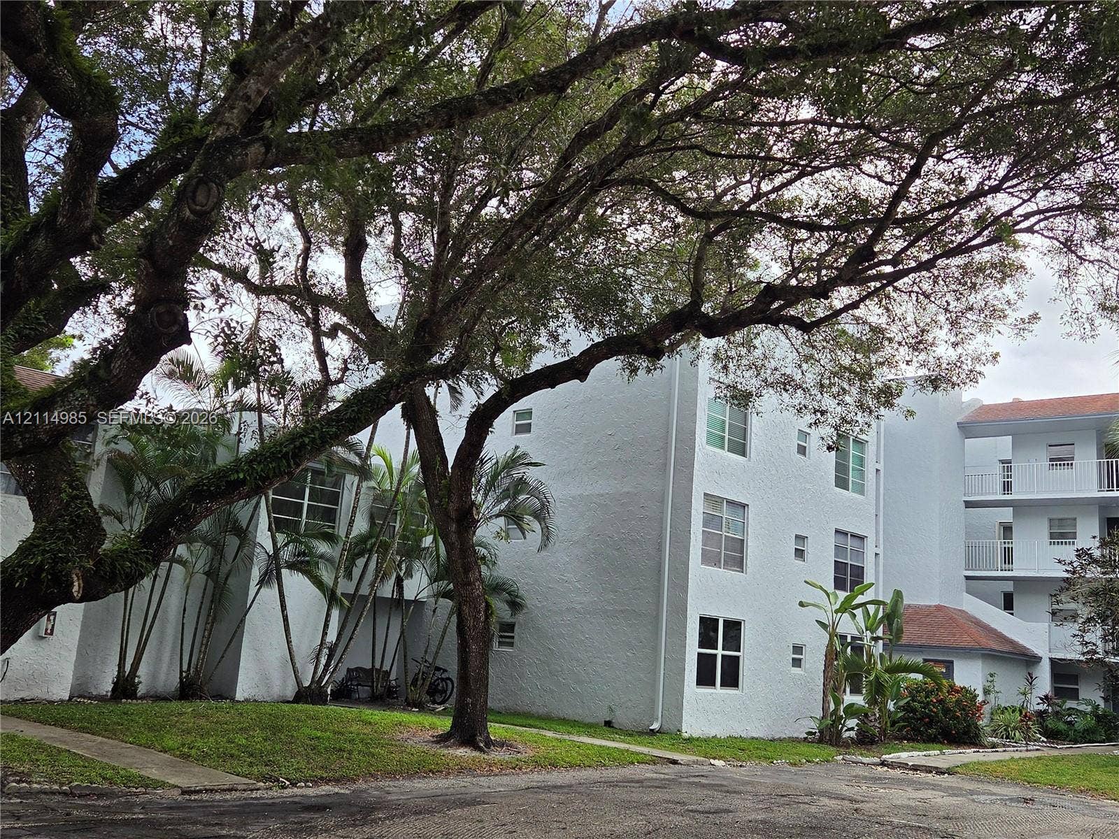 9441 Live Oak Place, #308, Davie, Davie, FL 33324 Multi-story building featuring textured stucco exterior, grid-pattern windows, multi-level exterior balconies with white railings, and mature trees