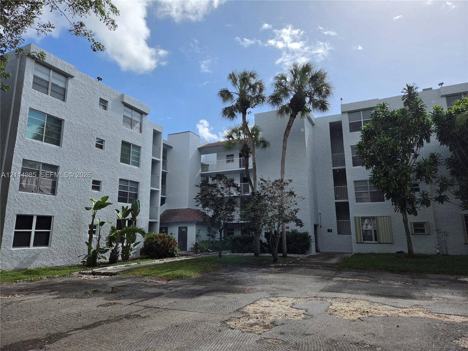 9441 Live Oak Place, #308, Davie, Davie, FL 33324 Multi-story residential building exterior featuring a textured stucco facade, asphalt parking area, and mature palm trees