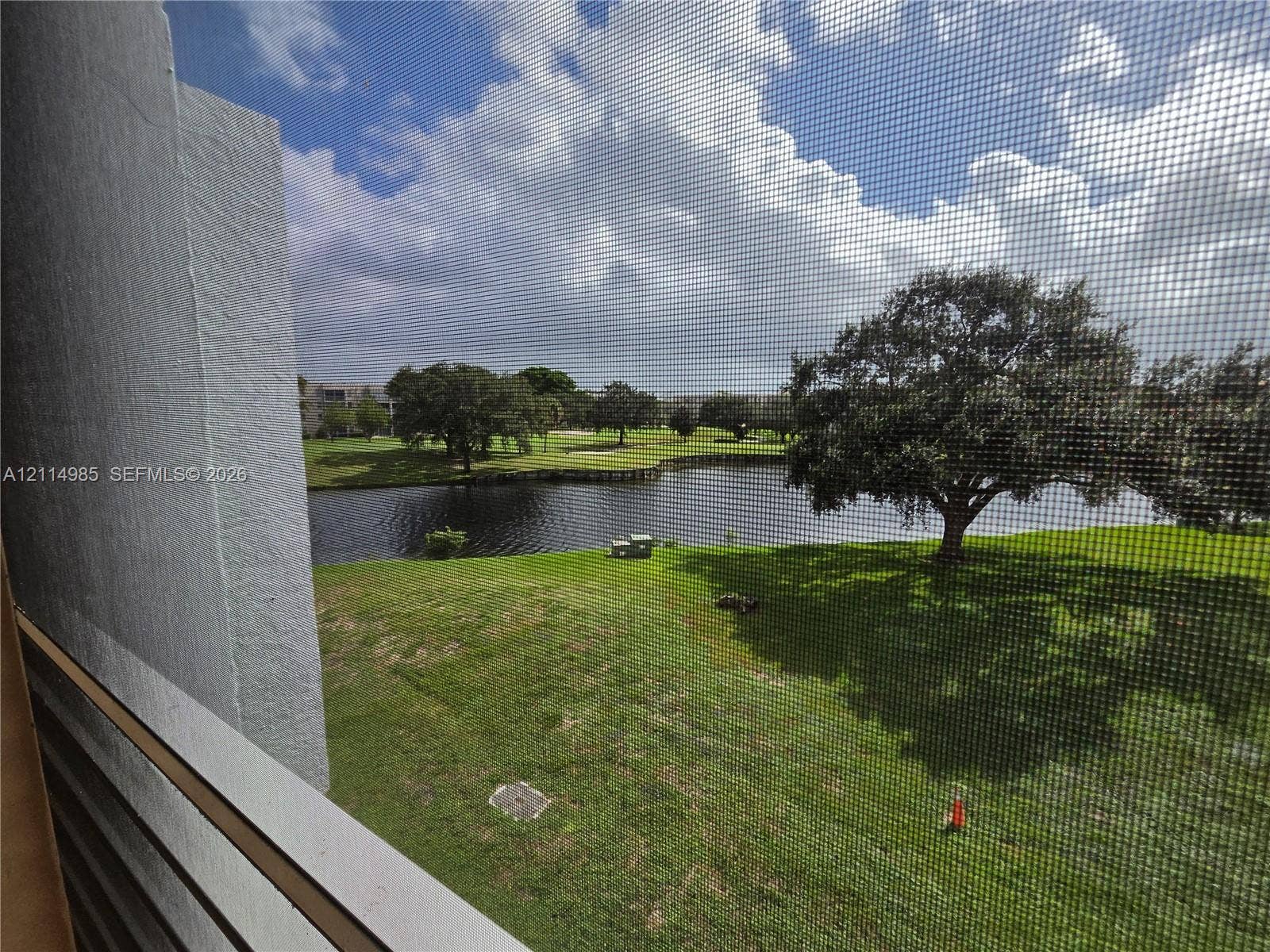 9441 Live Oak Place, #308, Davie, Davie, FL 33324 Exterior balcony featuring a white metal railing and a mesh screen overlooking a grass lawn, a pond, and mature trees