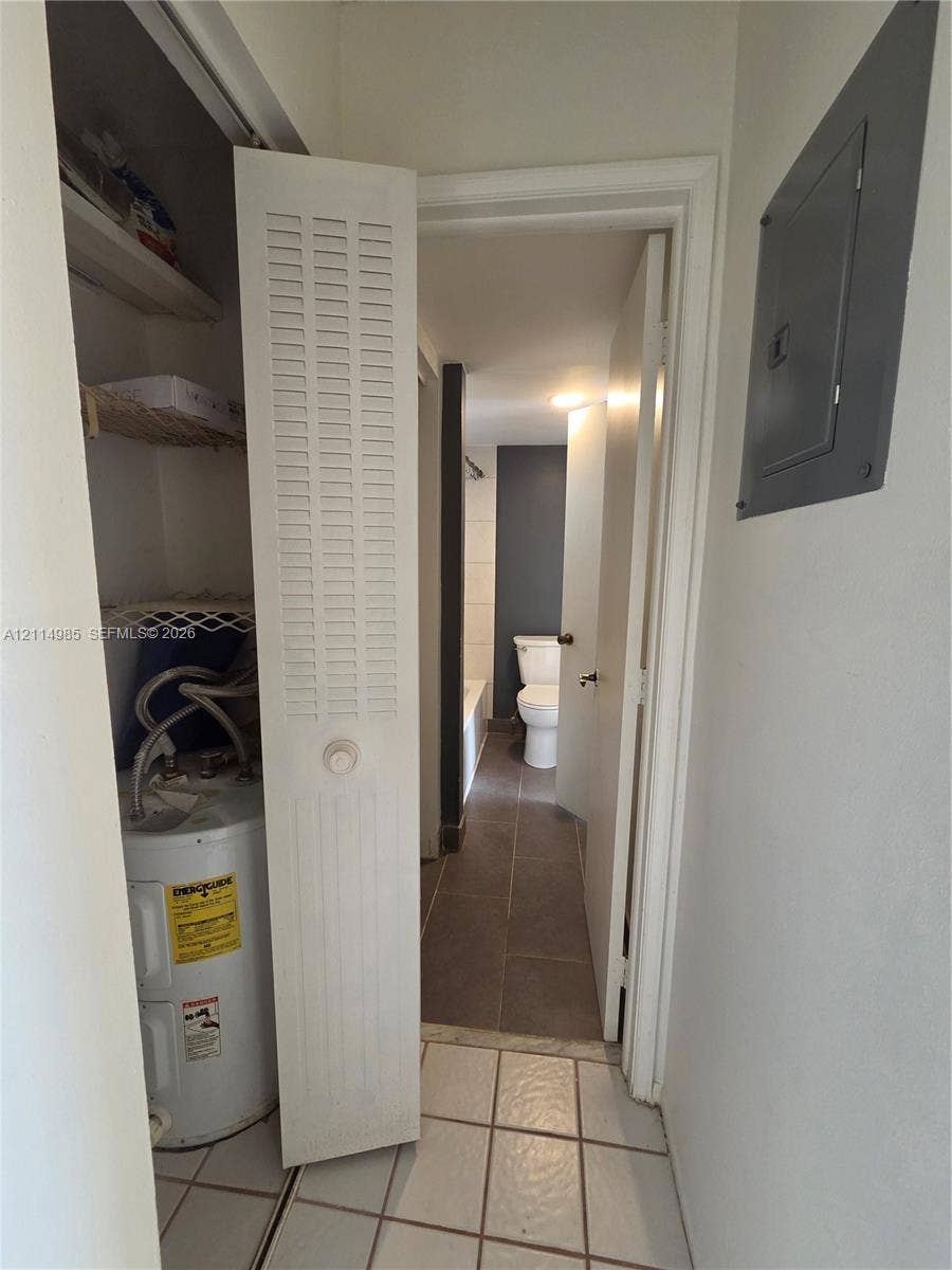 9441 Live Oak Place, #308, Davie, Davie, FL 33324 Utility closet featuring a louvered door, integrated shelving, and a water heater, with large-format tile flooring and an electrical service panel