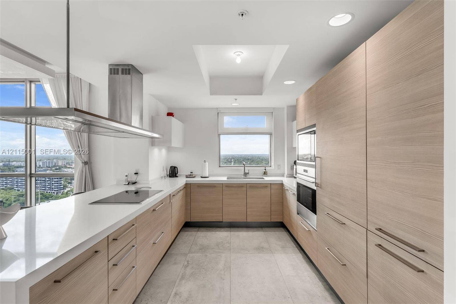 Kitchen featuring light-tone wood-finish cabinetry, white countertops, recessed lighting, a stainless steel range hood, and large-format tile flooring