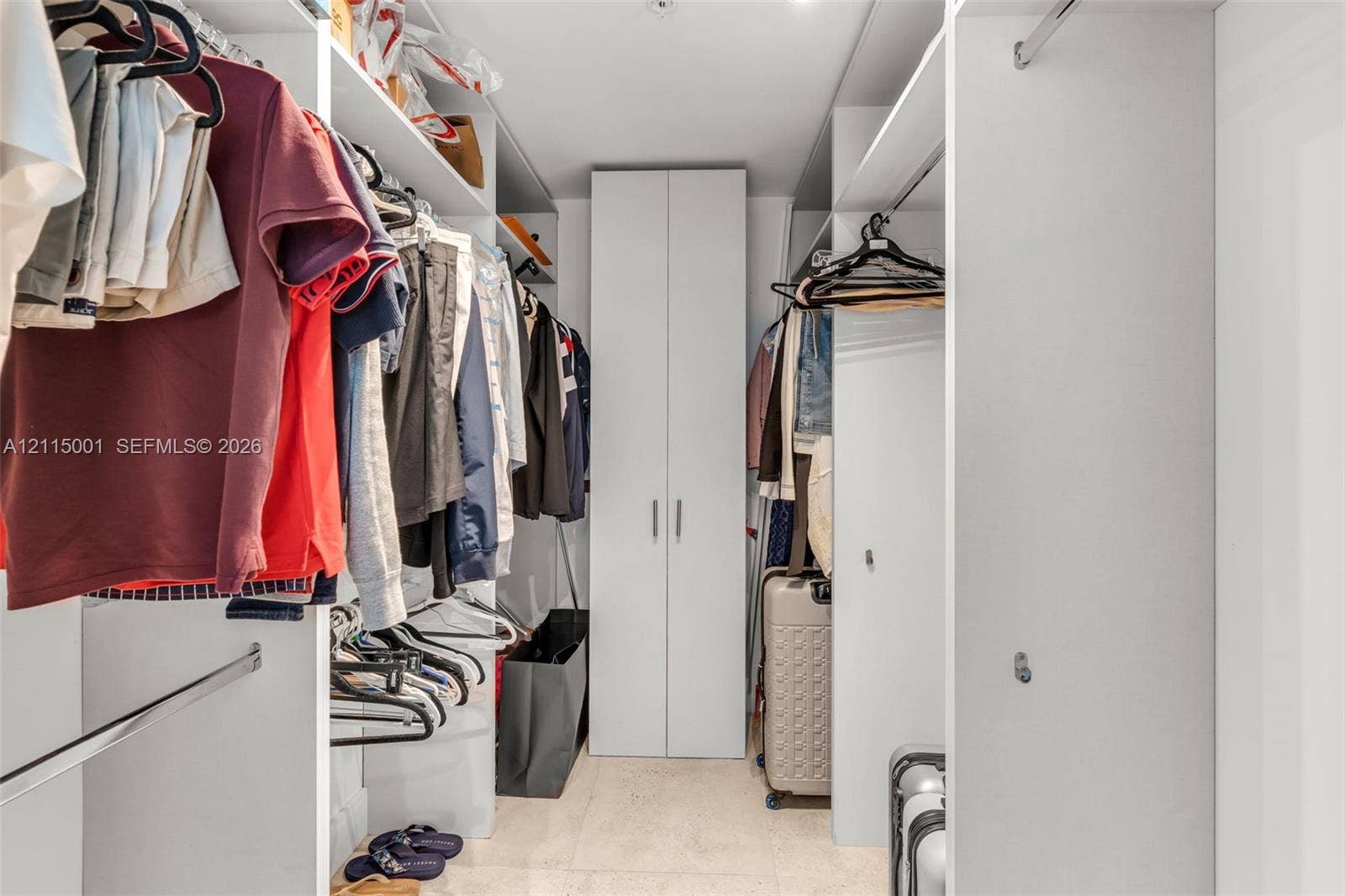 Walk-in closet featuring white built-in shelving, vertical storage cabinetry, and integrated metal clothing rods