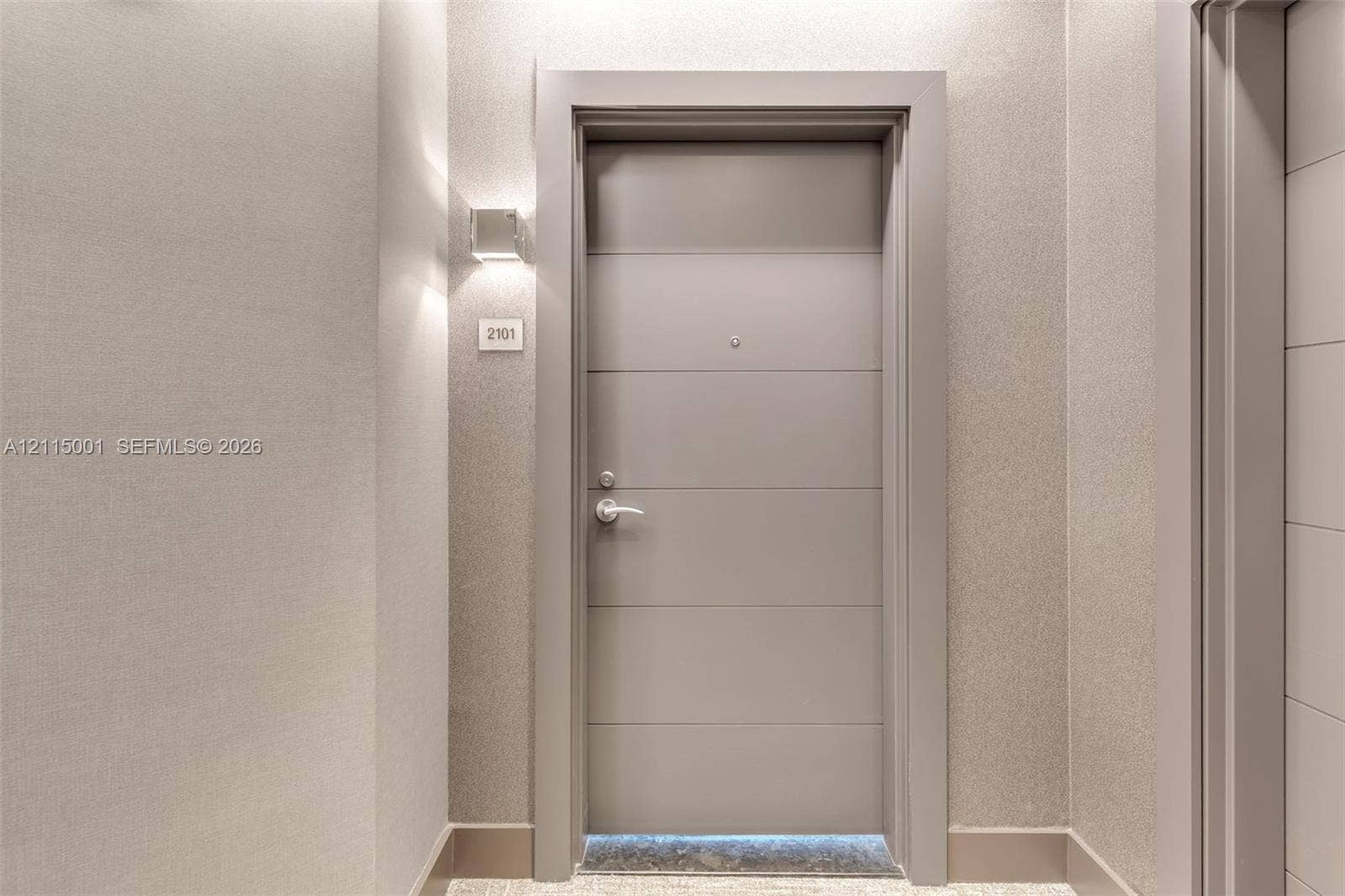 Solid-core entry door featuring horizontal panel detailing, metallic-finish hardware, peephole, and integrated wall-mounted sconce lighting
