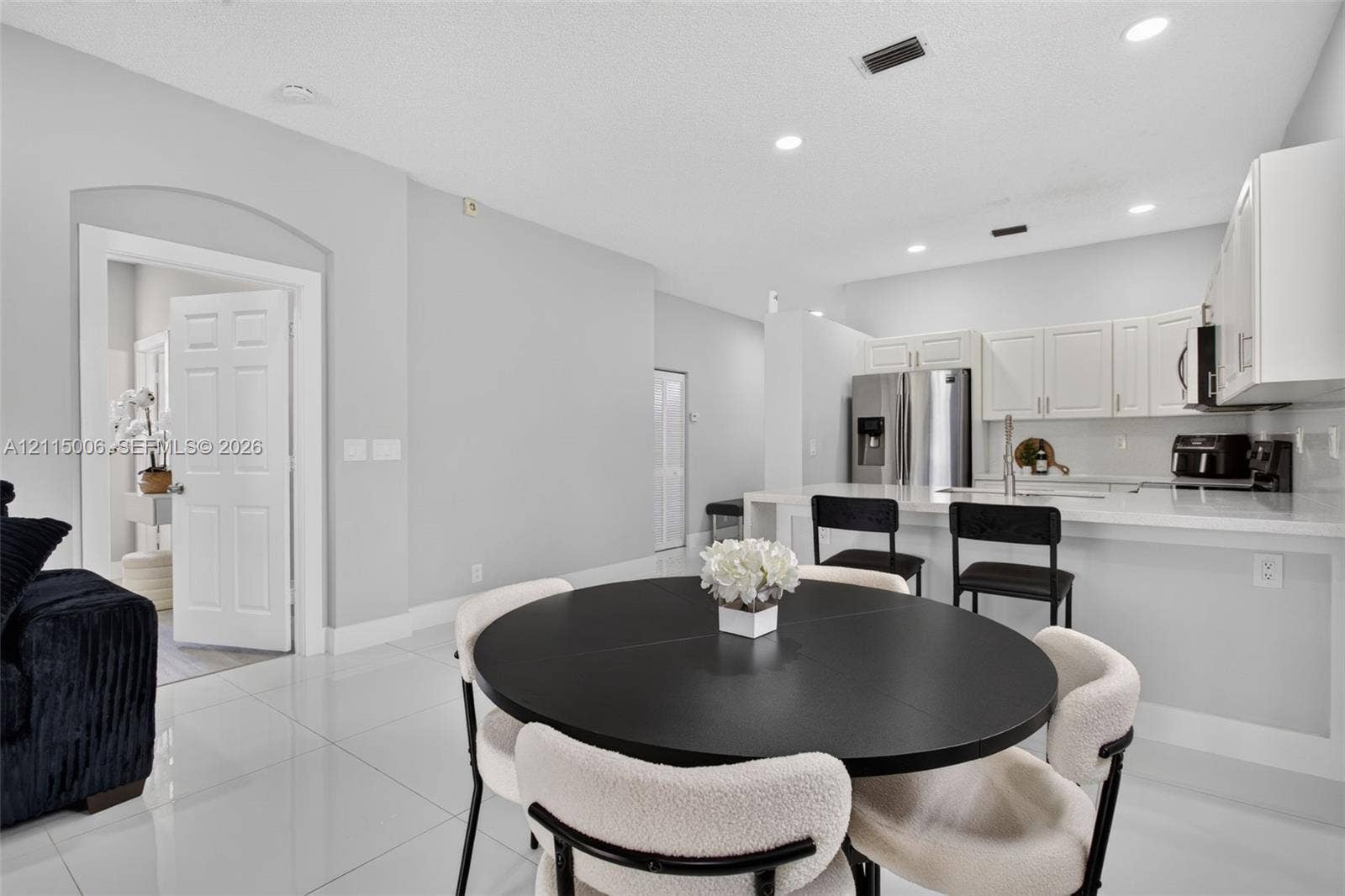 4812 NW 19th Street, Coconut Creek, FL 33063 Kitchen featuring white cabinetry, solid-surface countertops, a stainless steel refrigerator, and recessed lighting, accented by light-toned tile flooring and an arched entryway