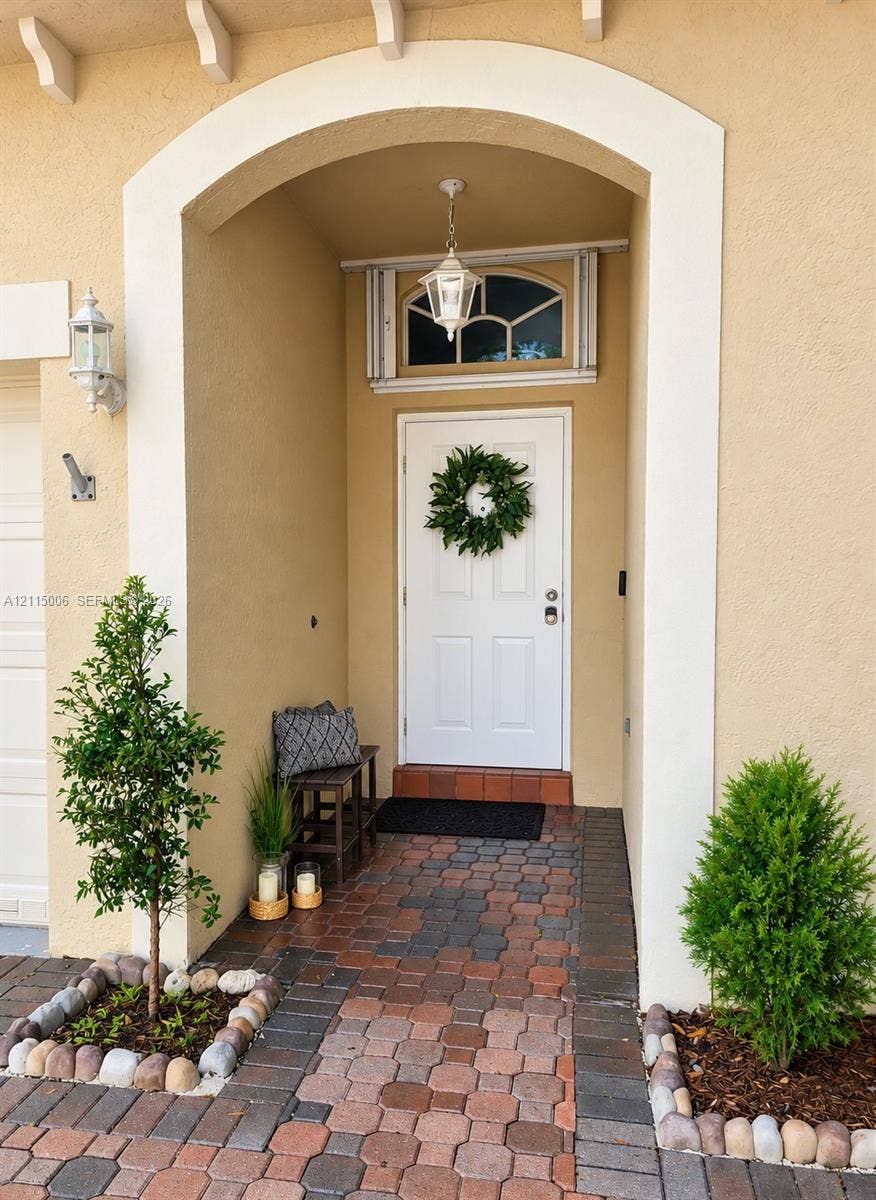 4812 NW 19th Street, Coconut Creek, FL 33063 Covered entryway featuring a recessed arched opening, decorative transom window, pendant lantern fixture, and multi-tonal paver hardscaping