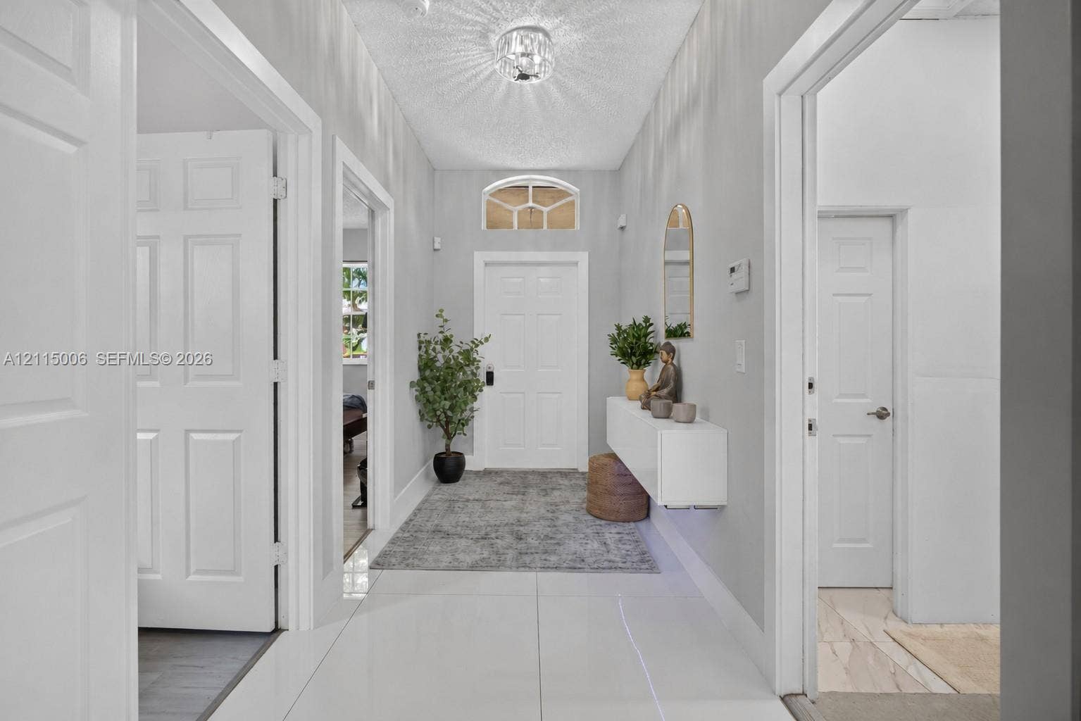 4812 NW 19th Street, Coconut Creek, FL 33063 Entryway featuring large-format tile flooring, a six-panel entry door with an arched transom window, a wall-mounted floating console, and a central crystal-style flush-mount light fixture