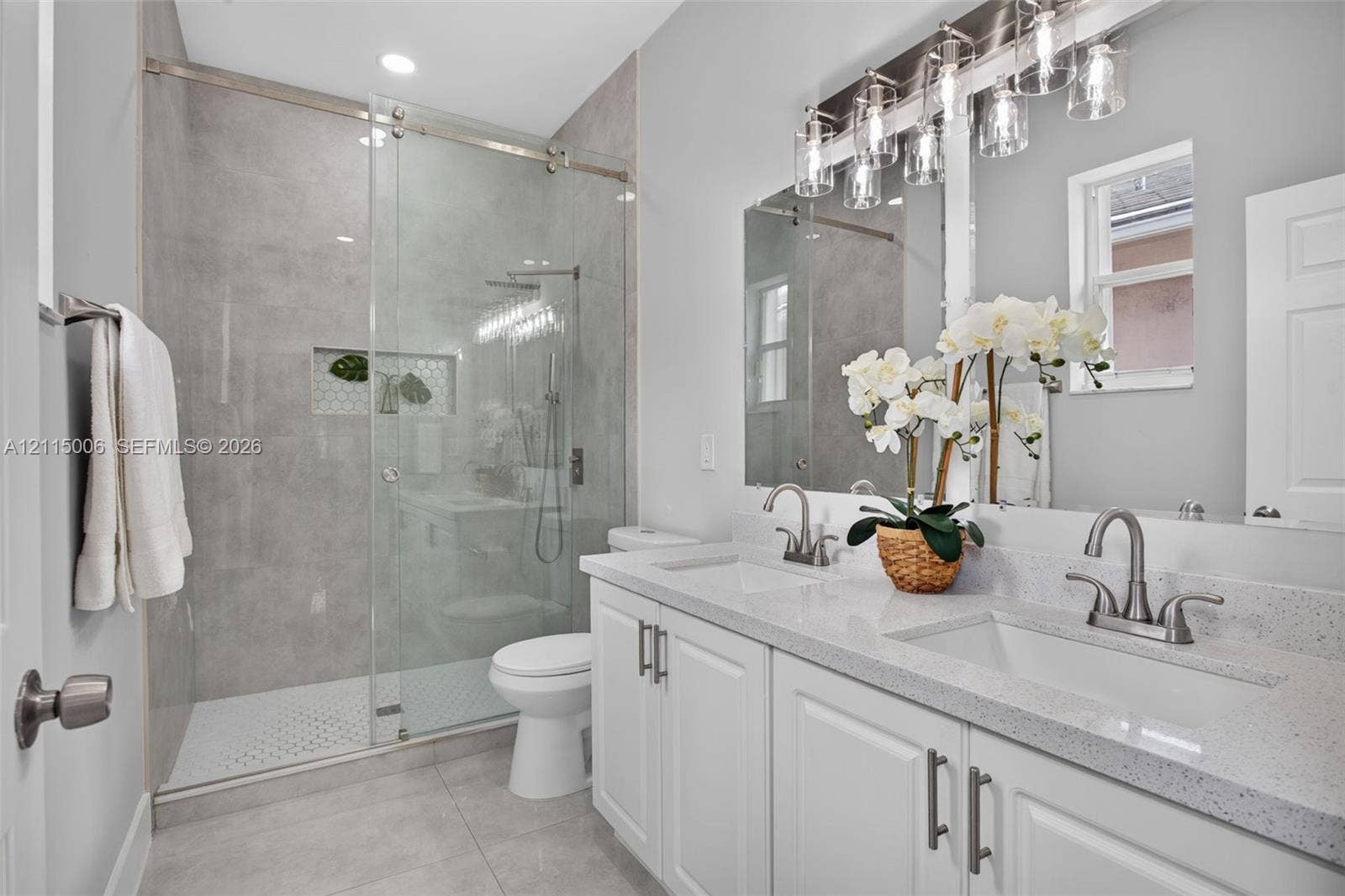 4812 NW 19th Street, Coconut Creek, FL 33063 Double vanity with light-colored composite countertops, walk-in shower with glass enclosure and tiled surround, recessed shower niche, and multi-light vanity fixture