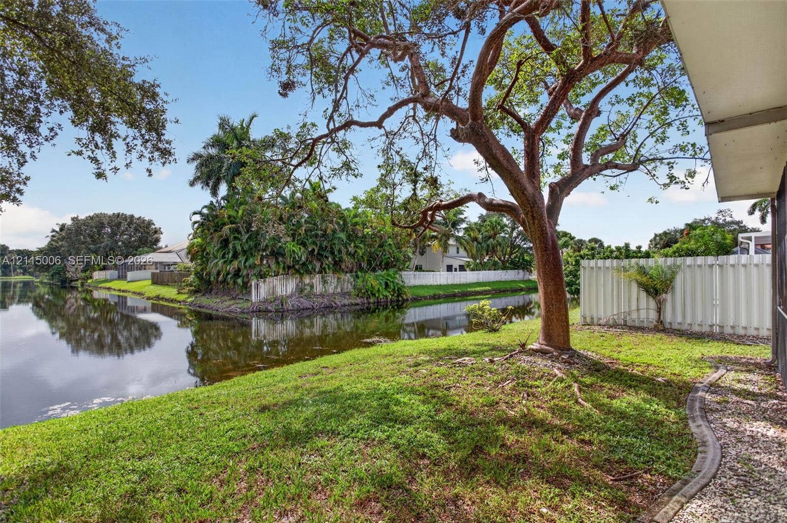 4812 NW 19th Street, Coconut Creek, FL 33063 Waterfront lot featuring mature trees, a grass lawn, and a vinyl privacy fence