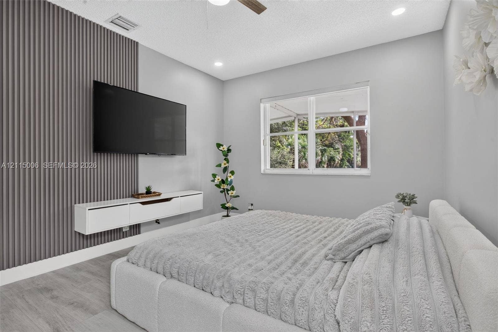 4812 NW 19th Street, Coconut Creek, FL 33063 Room featuring wood-finish flooring, a charcoal-toned vertical slat accent wall, a white wall-mounted floating media console, and a large multi-pane window